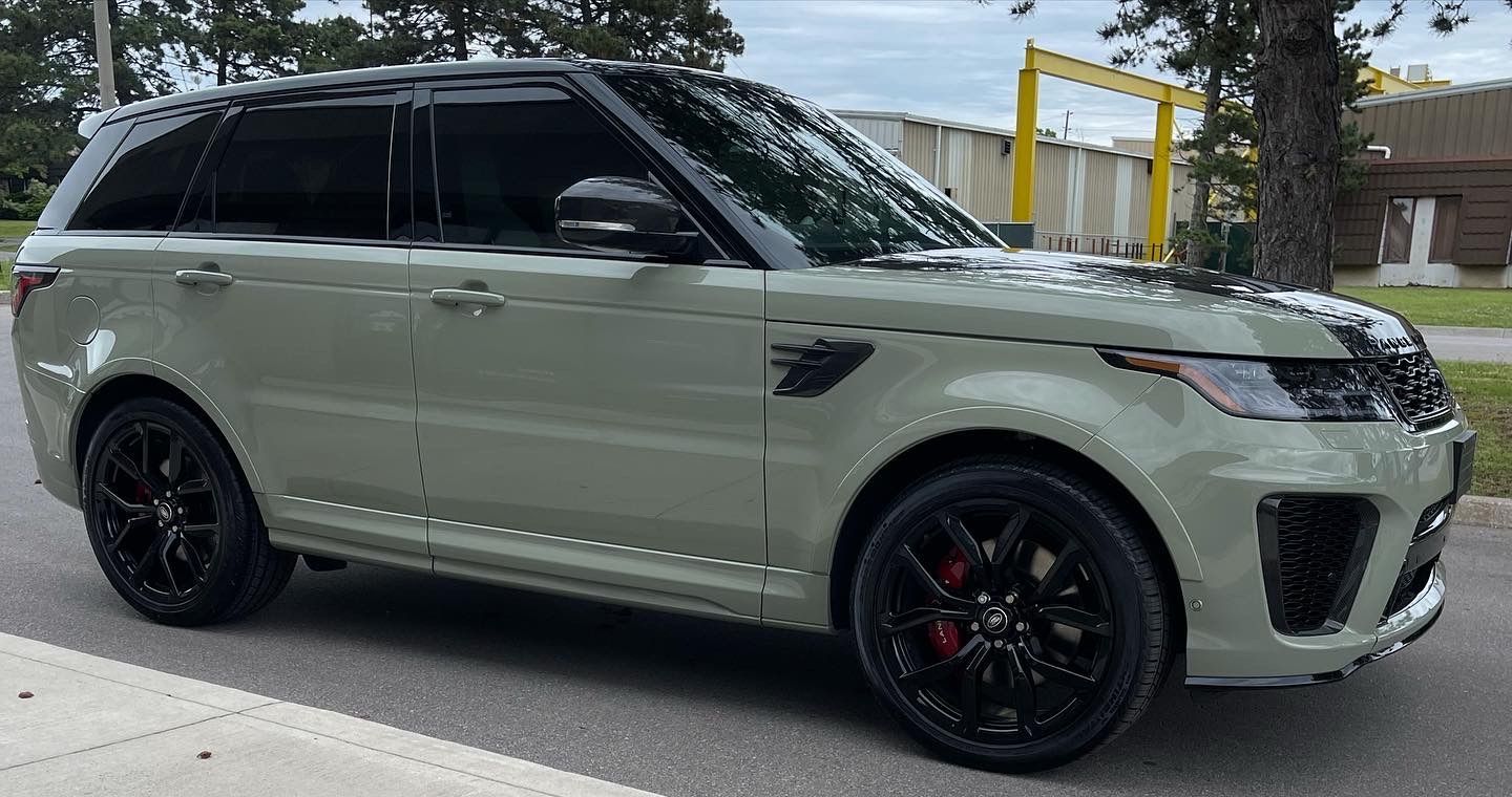 A sage green Land Rover Range Rover Sport with black wheels and a black roof parked outdoors.