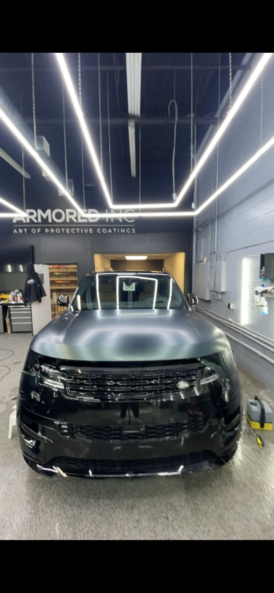 A Range Rover with a matte black hood and glossy black grille parked inside a professional automotive workshop.