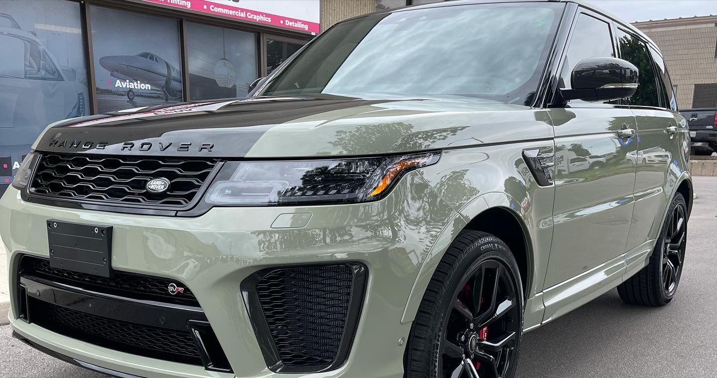 A sage green Land Rover Range Rover Sport parked outside a commercial building.