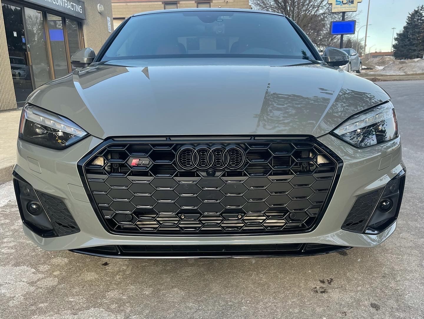A Nardo gray Audi S5 sedan parked outdoors, featuring a glossy black honeycomb front grille and darkened headlights.