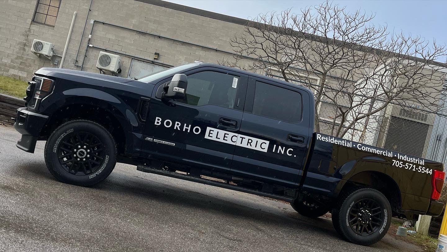A dark-colored pickup truck with Borho Electric Inc. branding, parked outside a building.