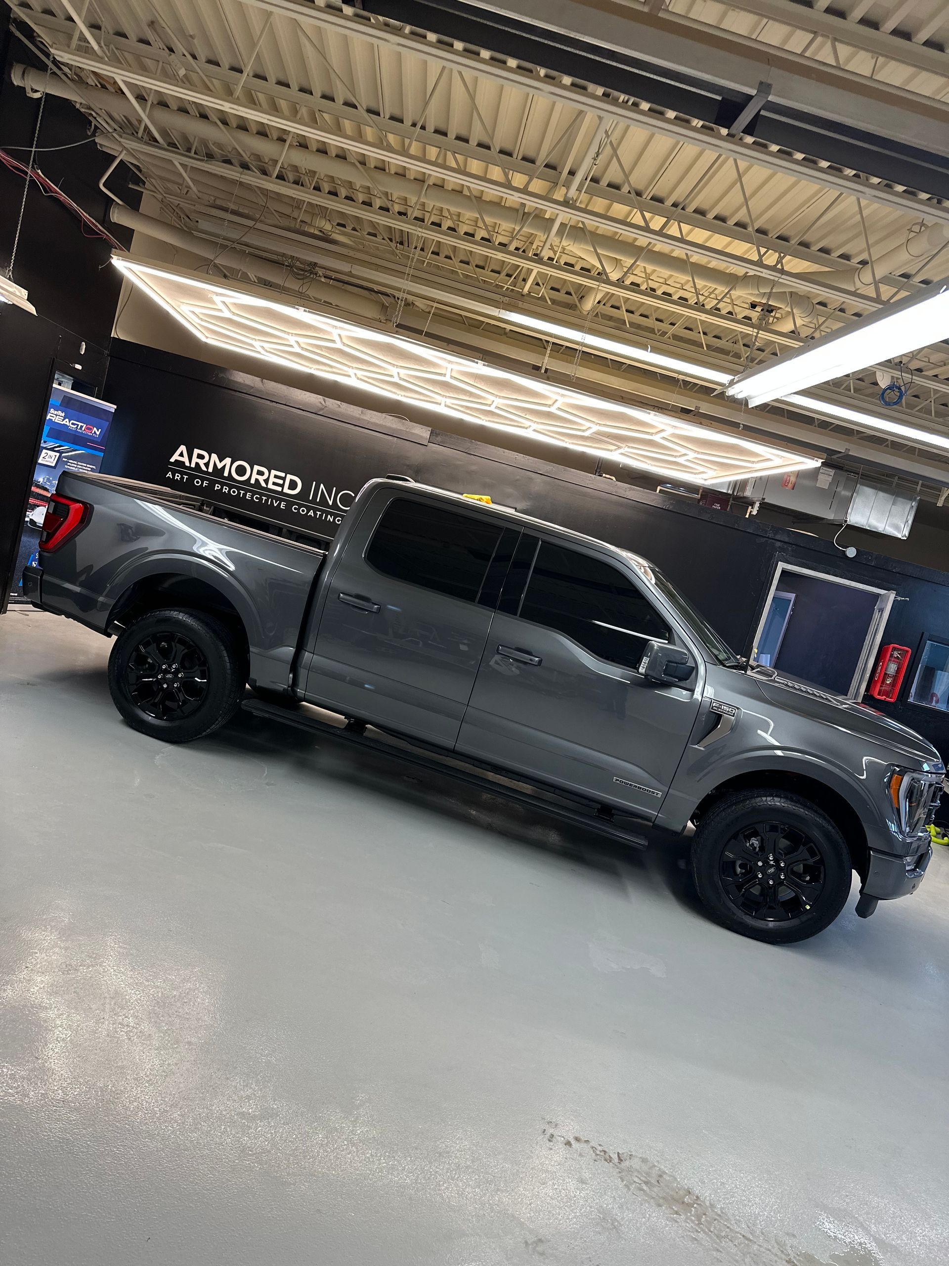 A gray Ford F-150 pickup truck with black wheels and tinted windows parked in a brightly lit showroom.