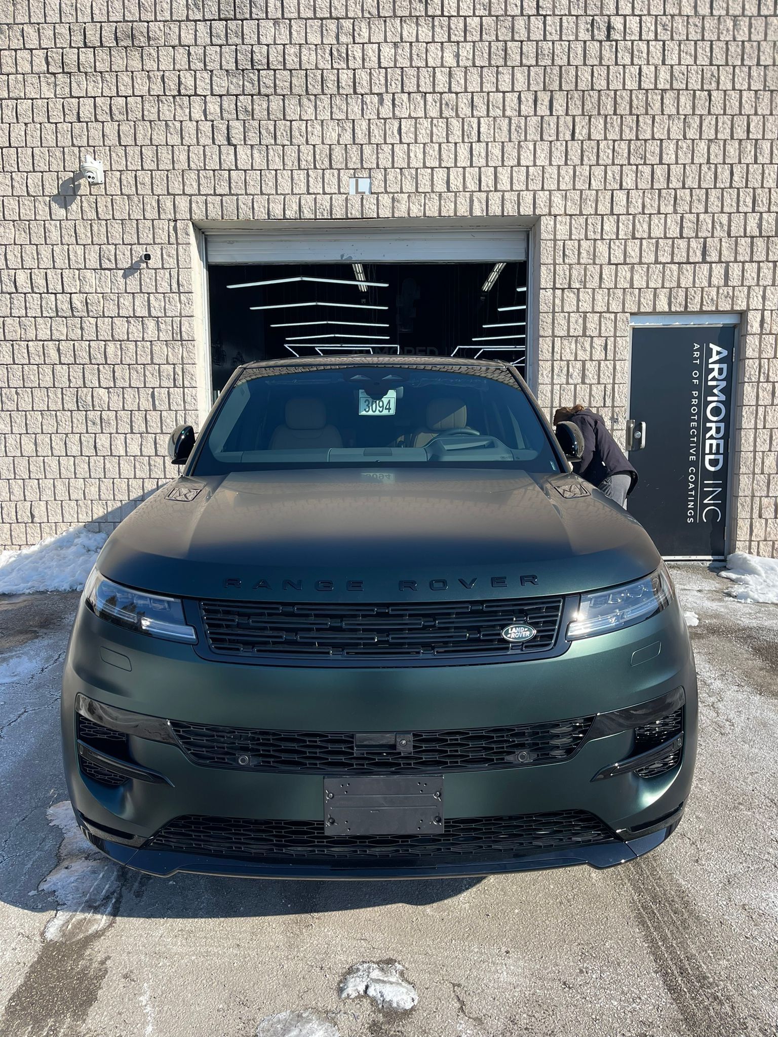 A matte dark green Range Rover parked outside a brick building with a sign that reads 