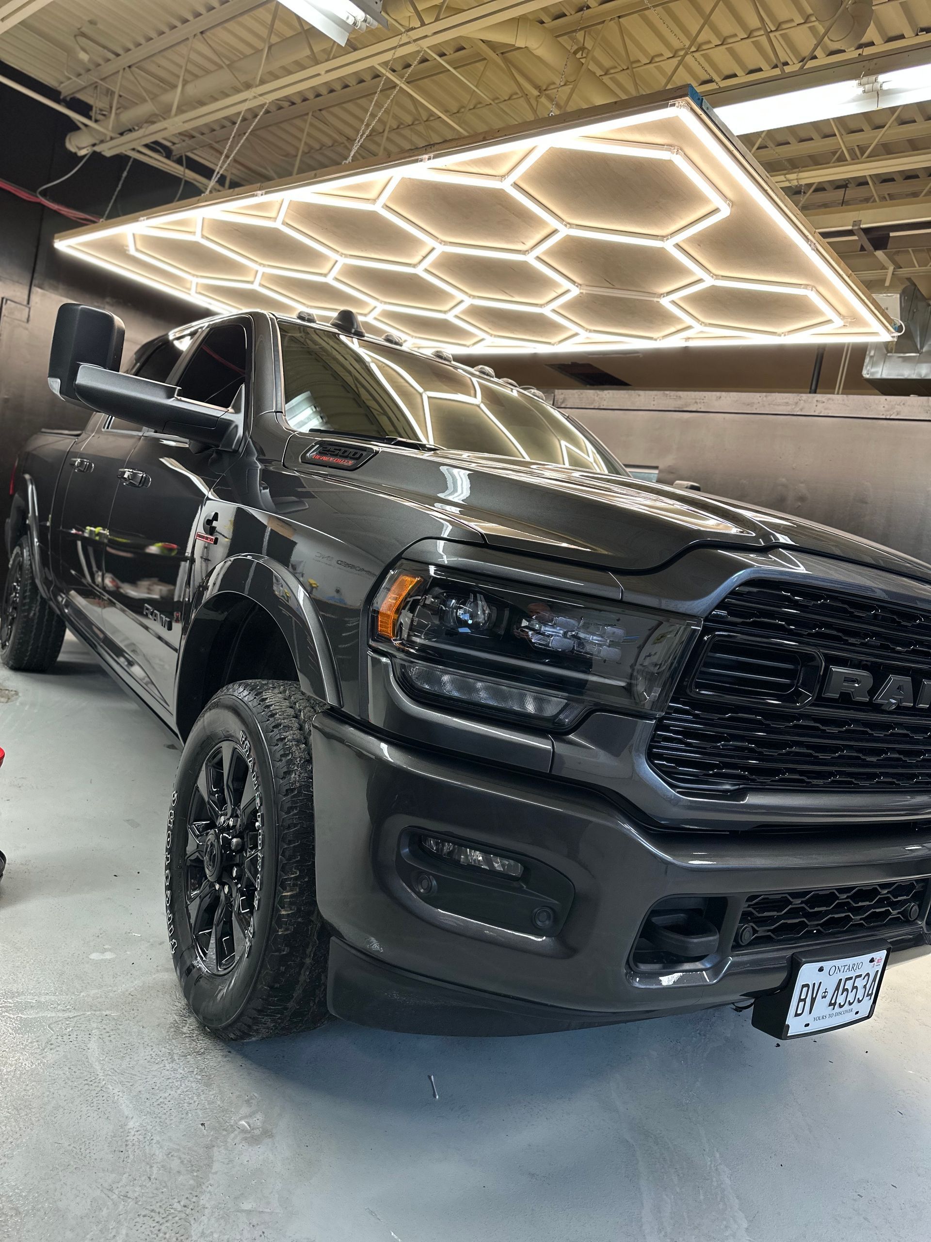 A dark gray Ram truck parked inside a garage under a large, glowing hexagonal light fixture.