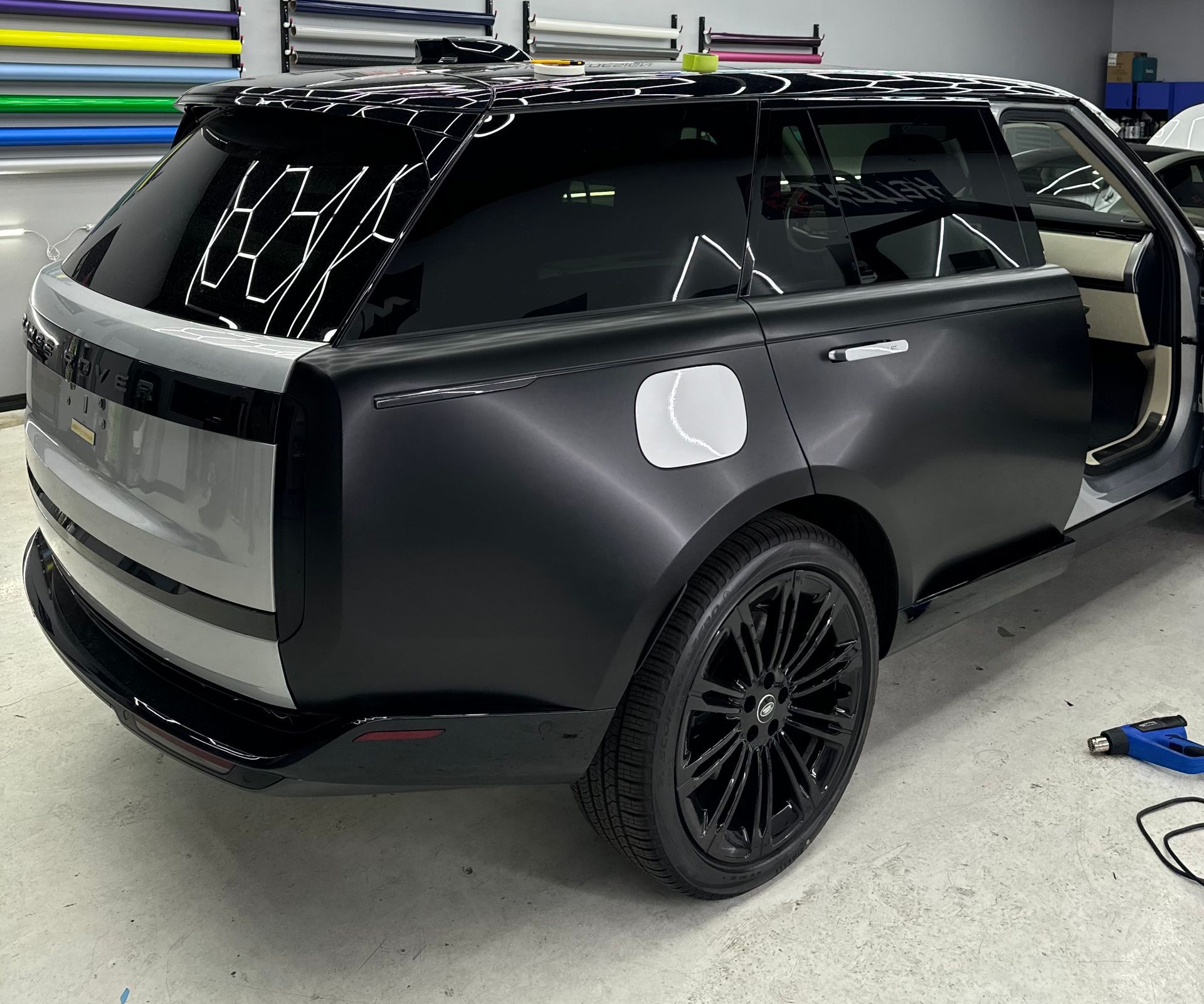 A Range Rover partially wrapped in matte black vinyl in a workshop, with a silver rear hatch and black alloy wheels.
