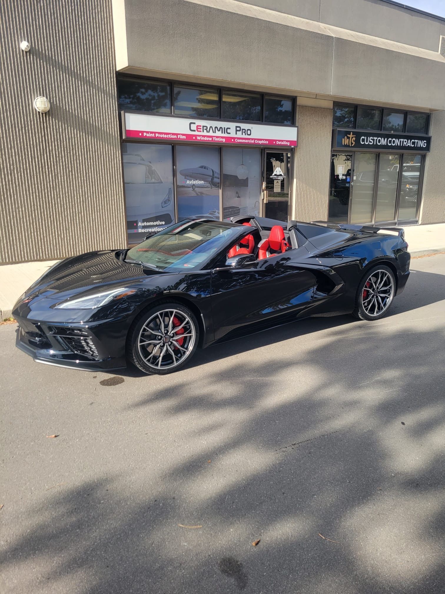 A black convertible Corvette sports car with red interior parked in front of a storefront.