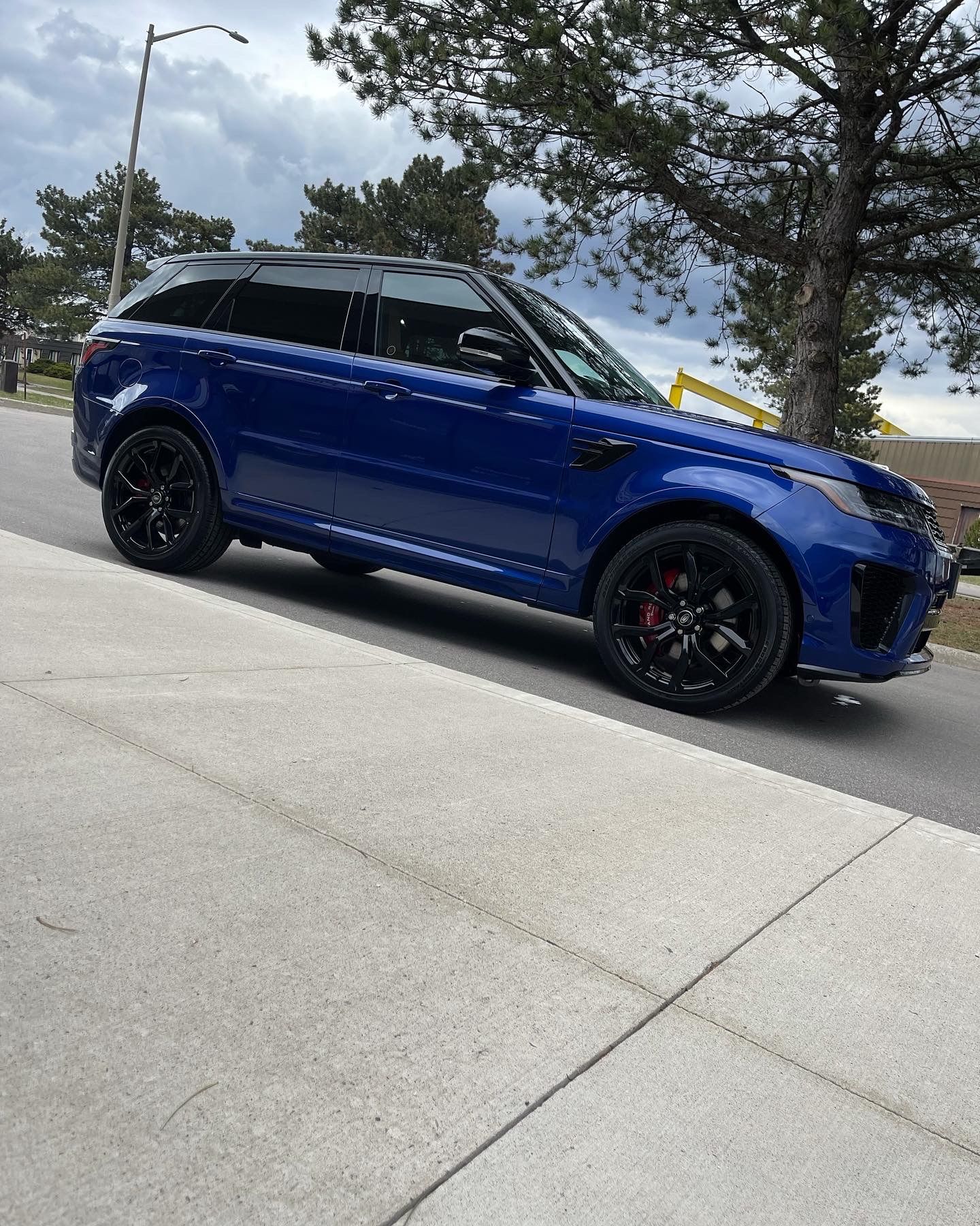 A vibrant blue Land Rover Range Rover Sport parked on a concrete street near trees and a utility pole.