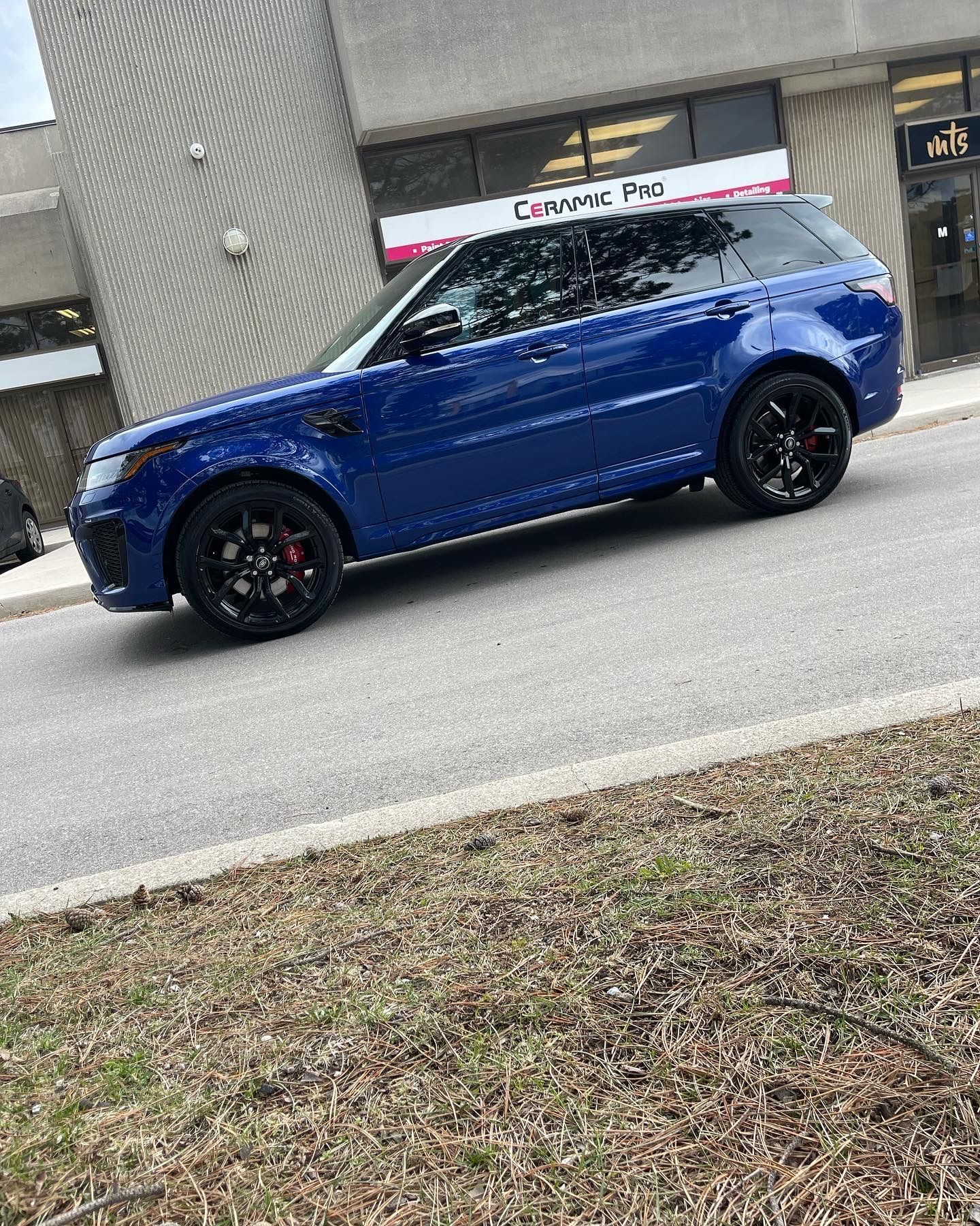 A bright blue Range Rover Sport SUV parked on a paved lot in front of a building storefront.