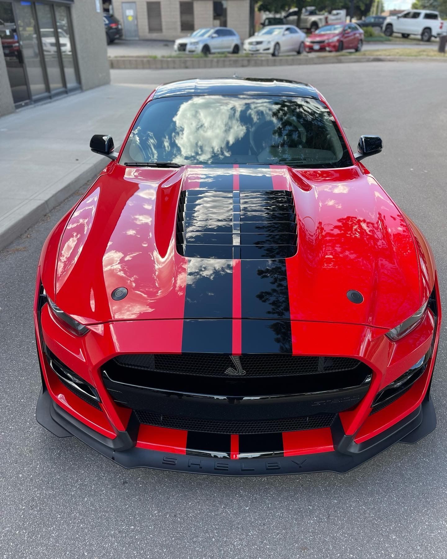 A bright red Ford Mustang Shelby GT500 with black racing stripes, parked on an asphalt lot.
