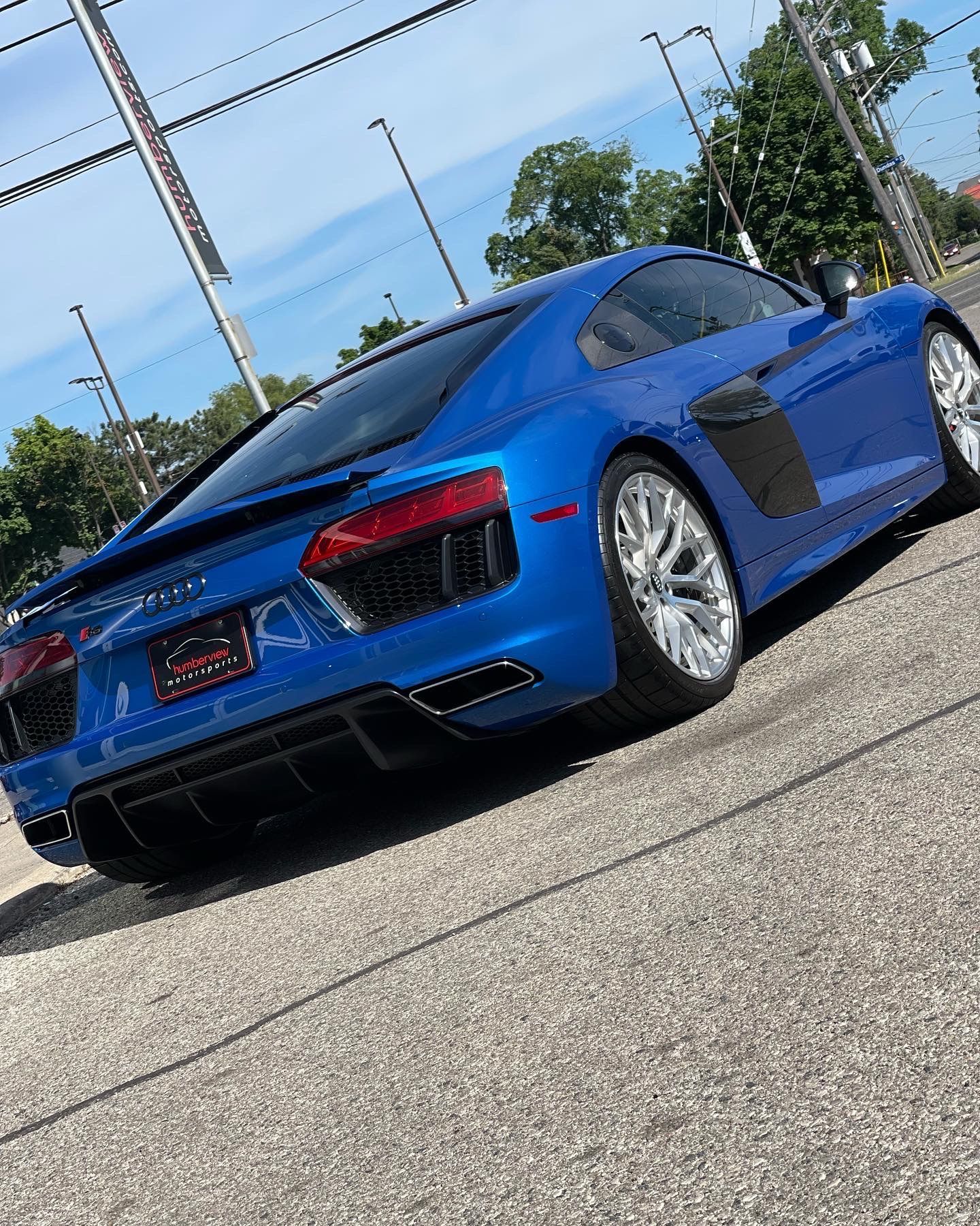 A bright blue Audi R8 sports car parked on an asphalt lot under a sunny sky.