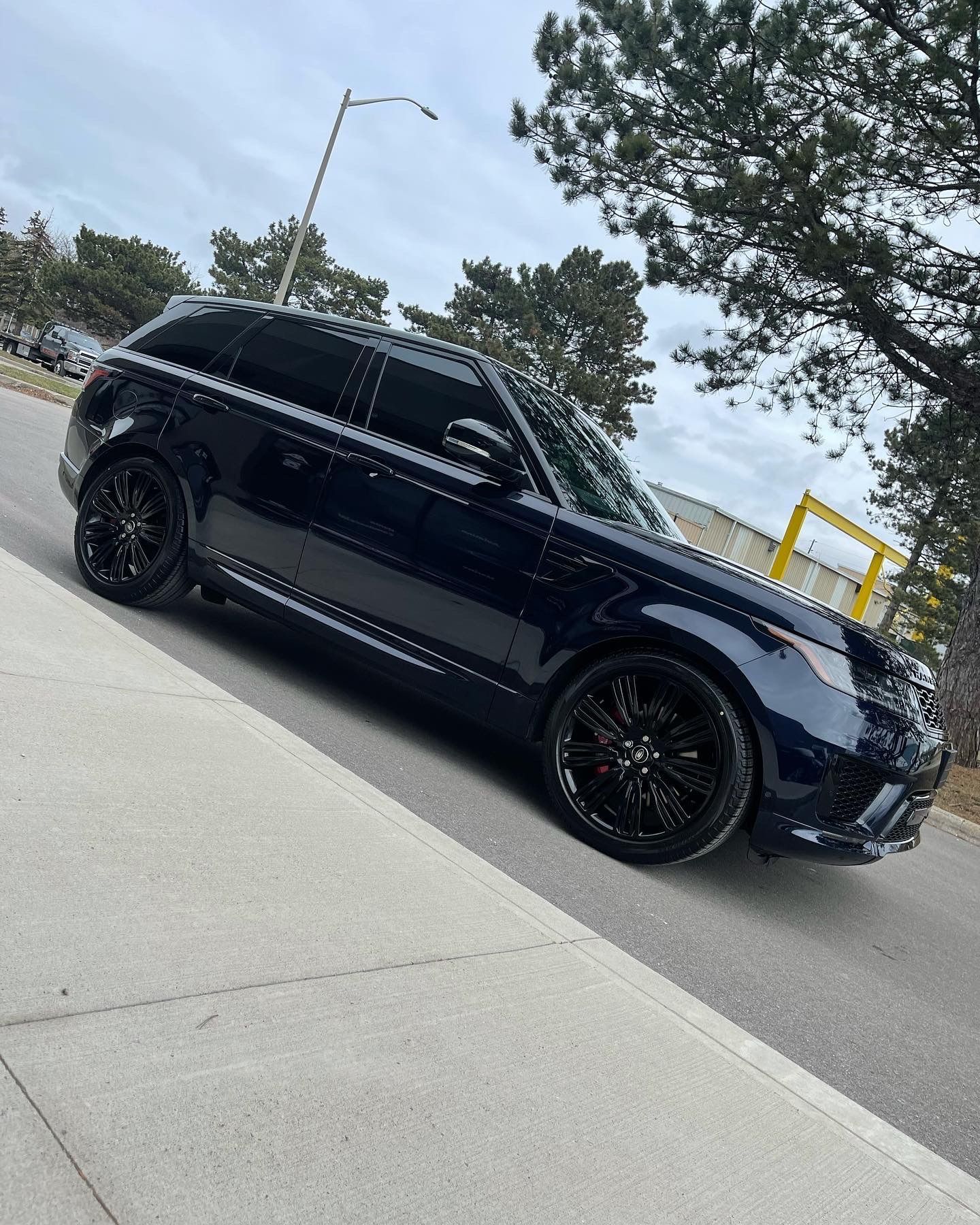 A sleek black Land Rover Range Rover parked on an asphalt road next to a sidewalk with trees in the background.