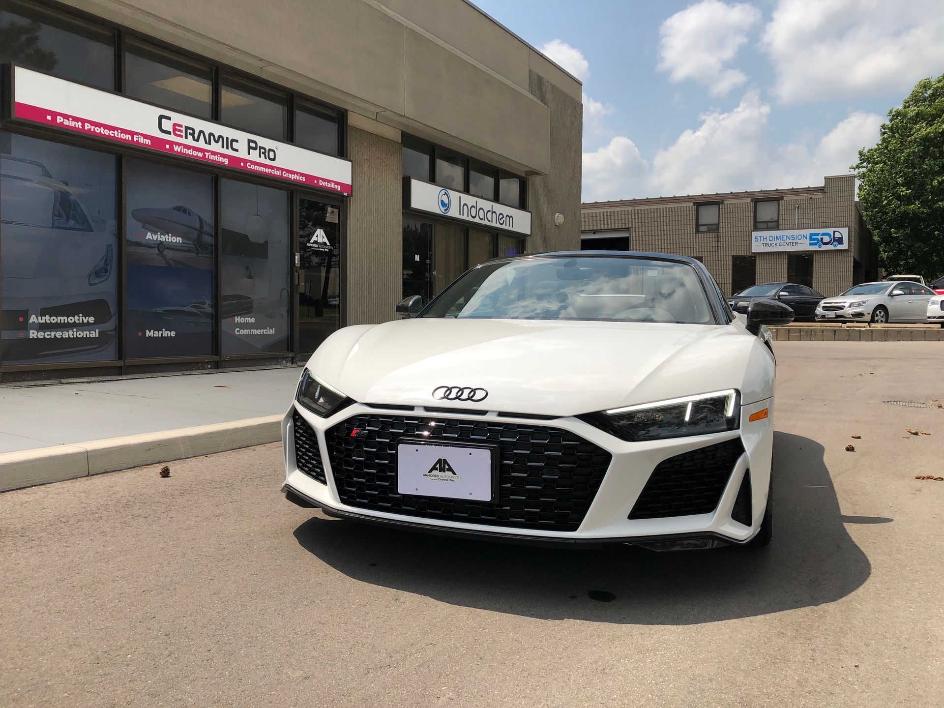 A white Audi R8 parked in front of a Ceramic Pro business under a sunny sky.