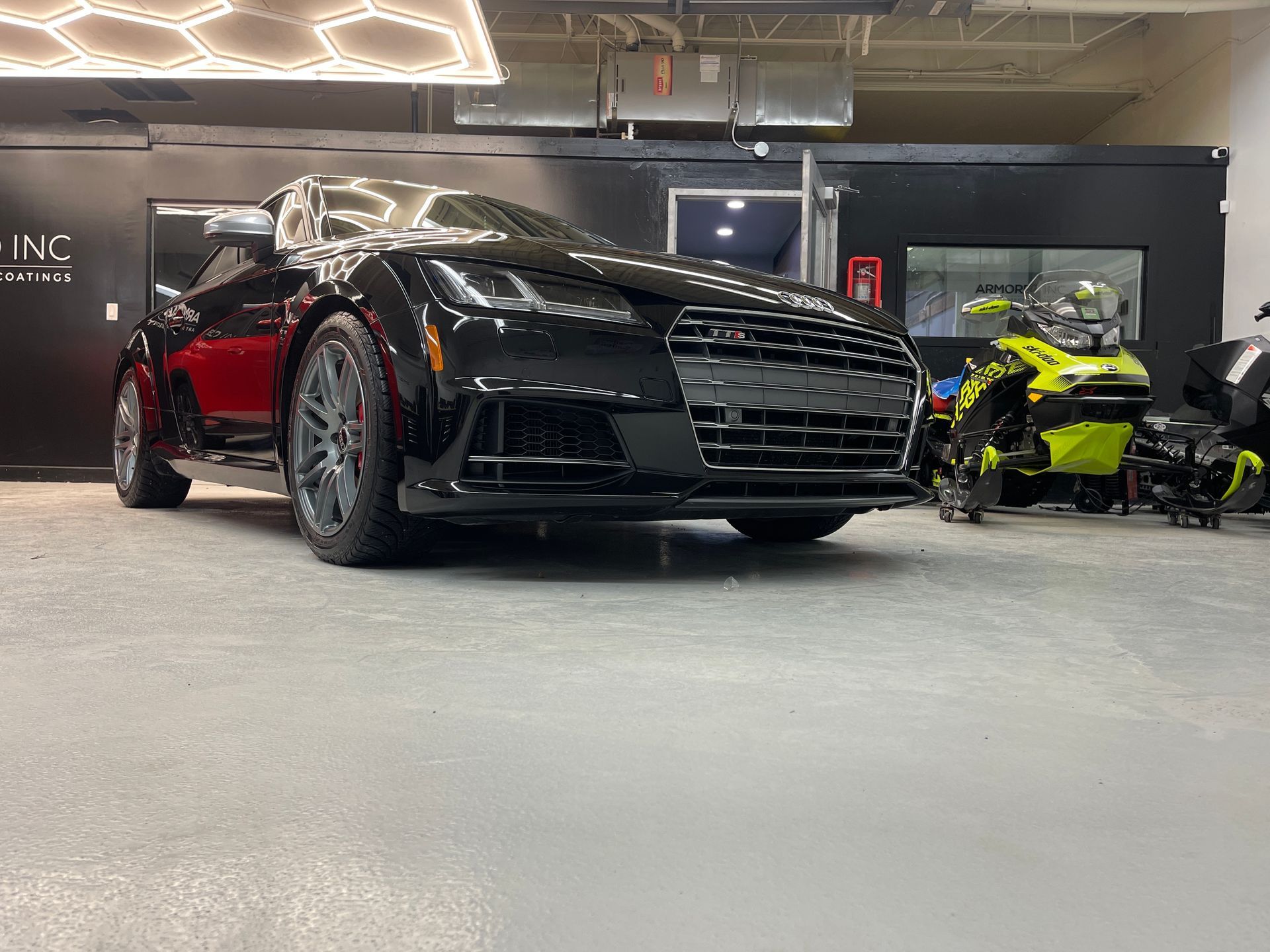 A black Audi sports car parked inside a garage next to a bright yellow snowmobile.