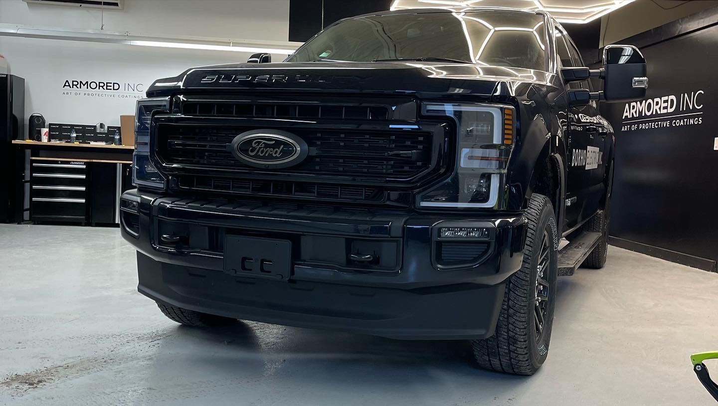 A black Ford Super Duty truck parked inside an automotive workshop with Armored Inc. branding on the wall.