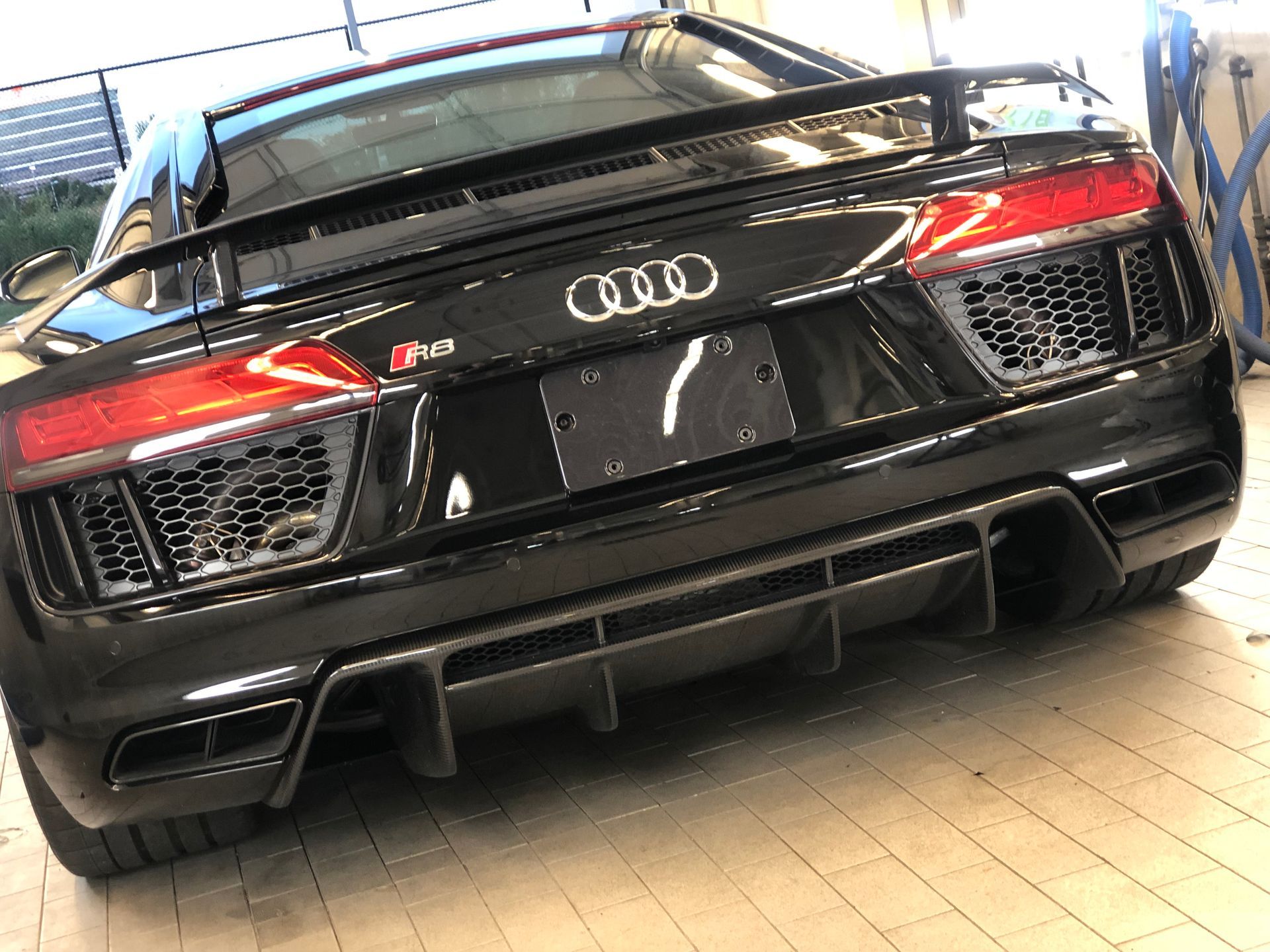 The rear view of a black Audi R8 sports car featuring a carbon fiber diffuser and rear wing inside a garage.