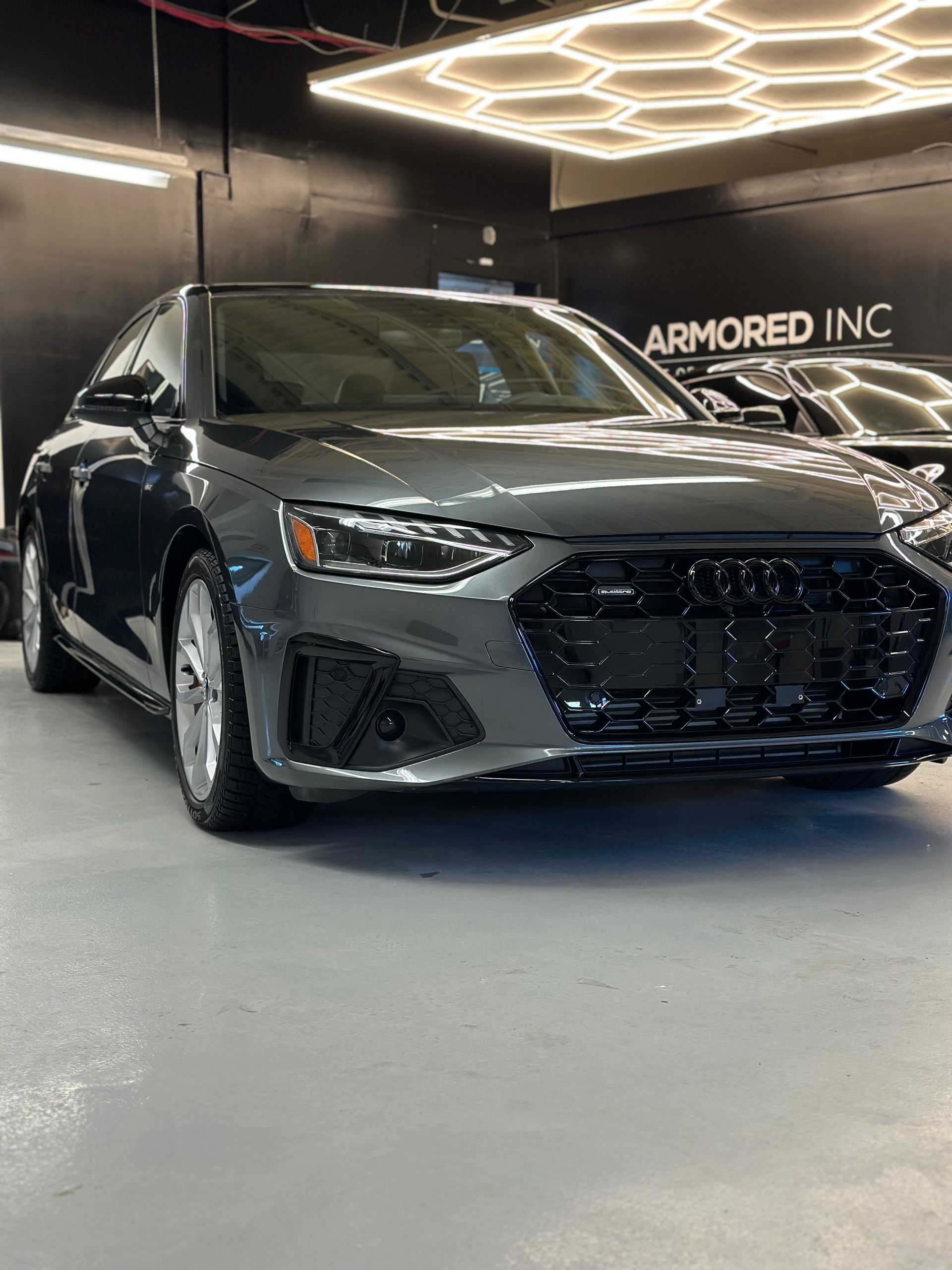 A gray Audi sedan parked indoors on a glossy floor under geometric LED lights, with 