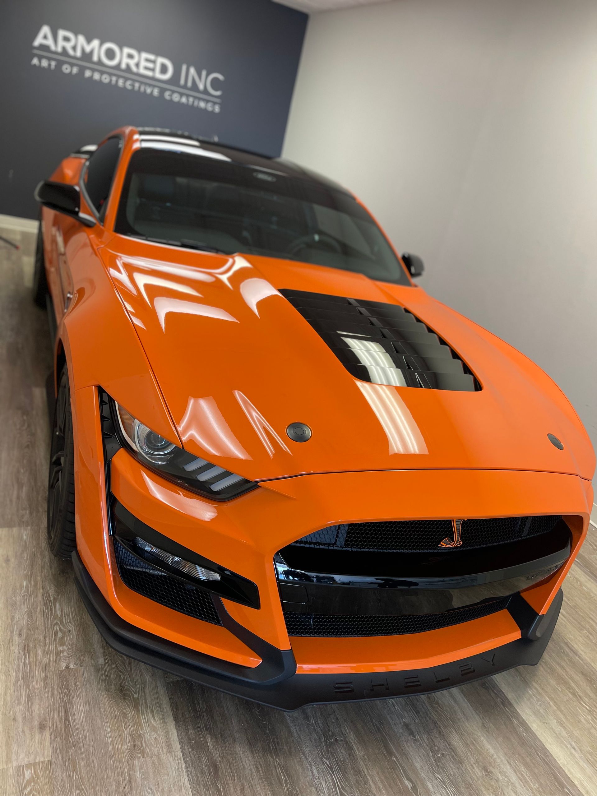 An orange Ford Mustang Shelby GT500 with a black racing stripe, parked in an 