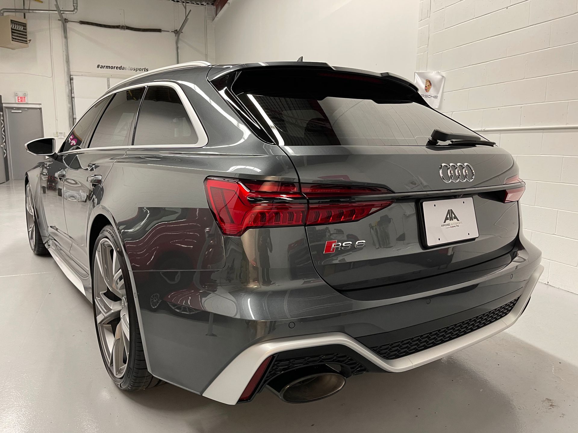 A dark gray Audi RS6 Avant wagon parked inside a bright, white-walled garage, seen from a rear three-quarter angle.