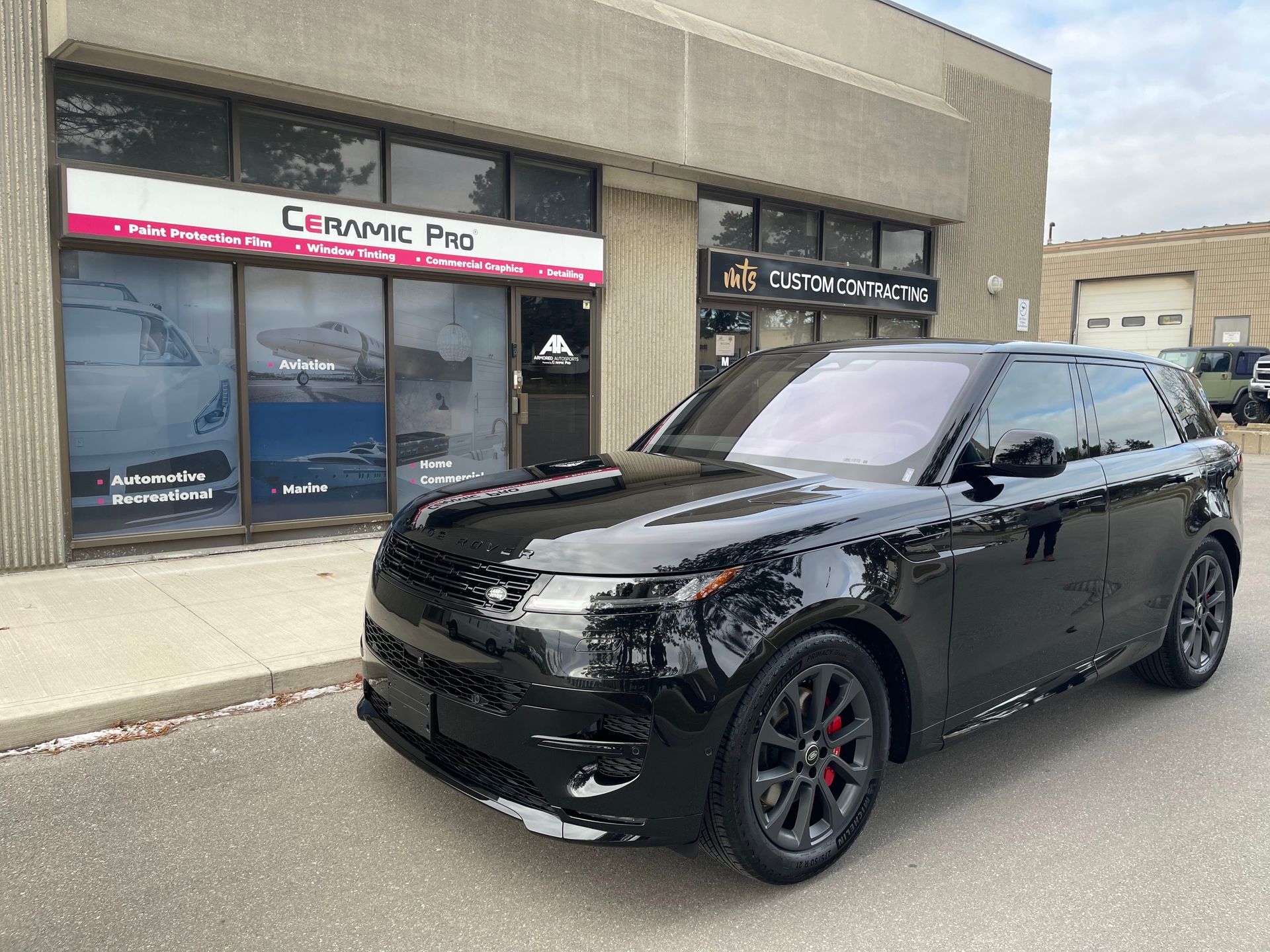 A black Land Rover parked in front of a Ceramic Pro detailing shop.