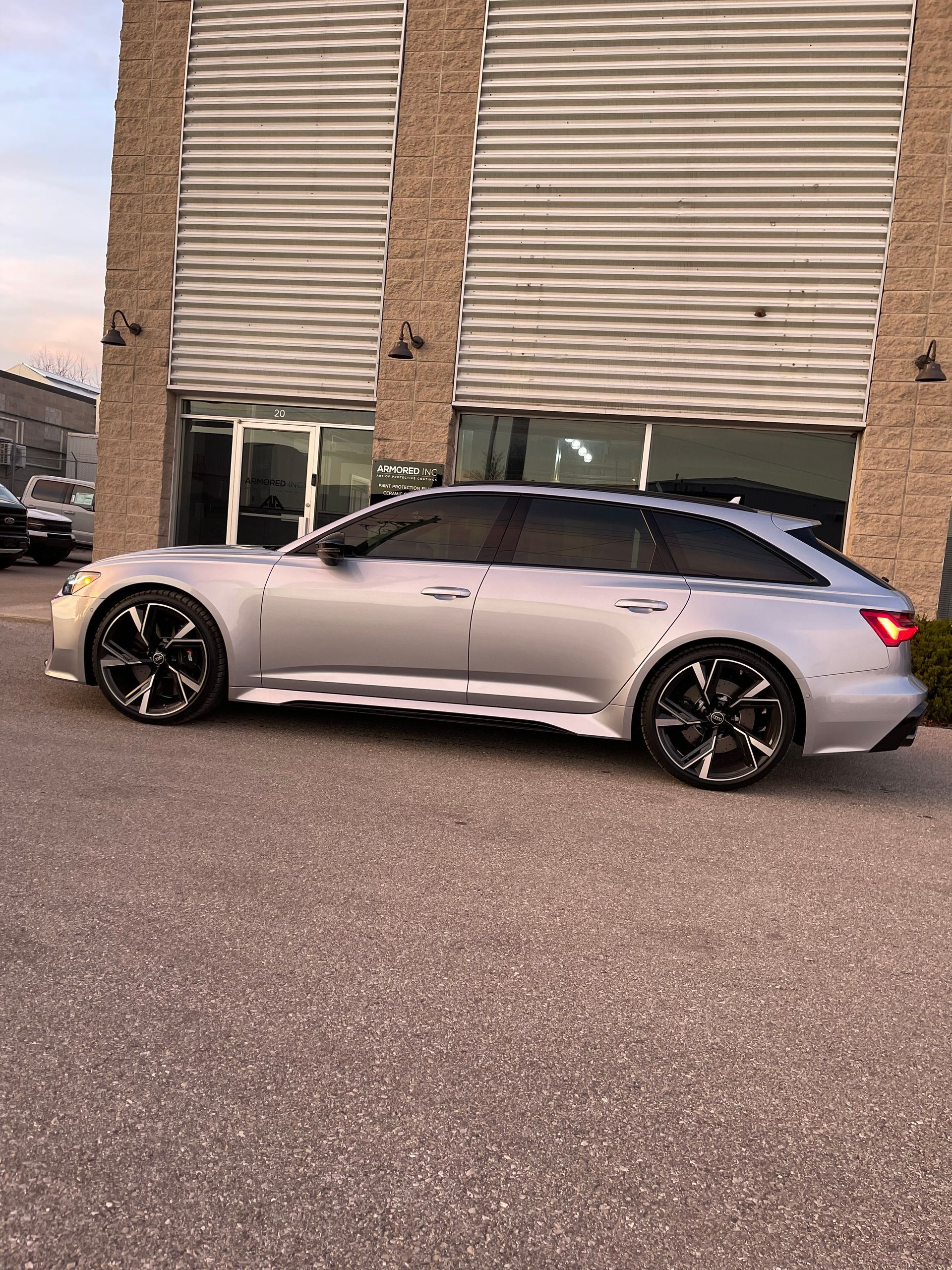 A silver Audi RS6 Avant parked on an asphalt lot in front of a building with corrugated metal siding.