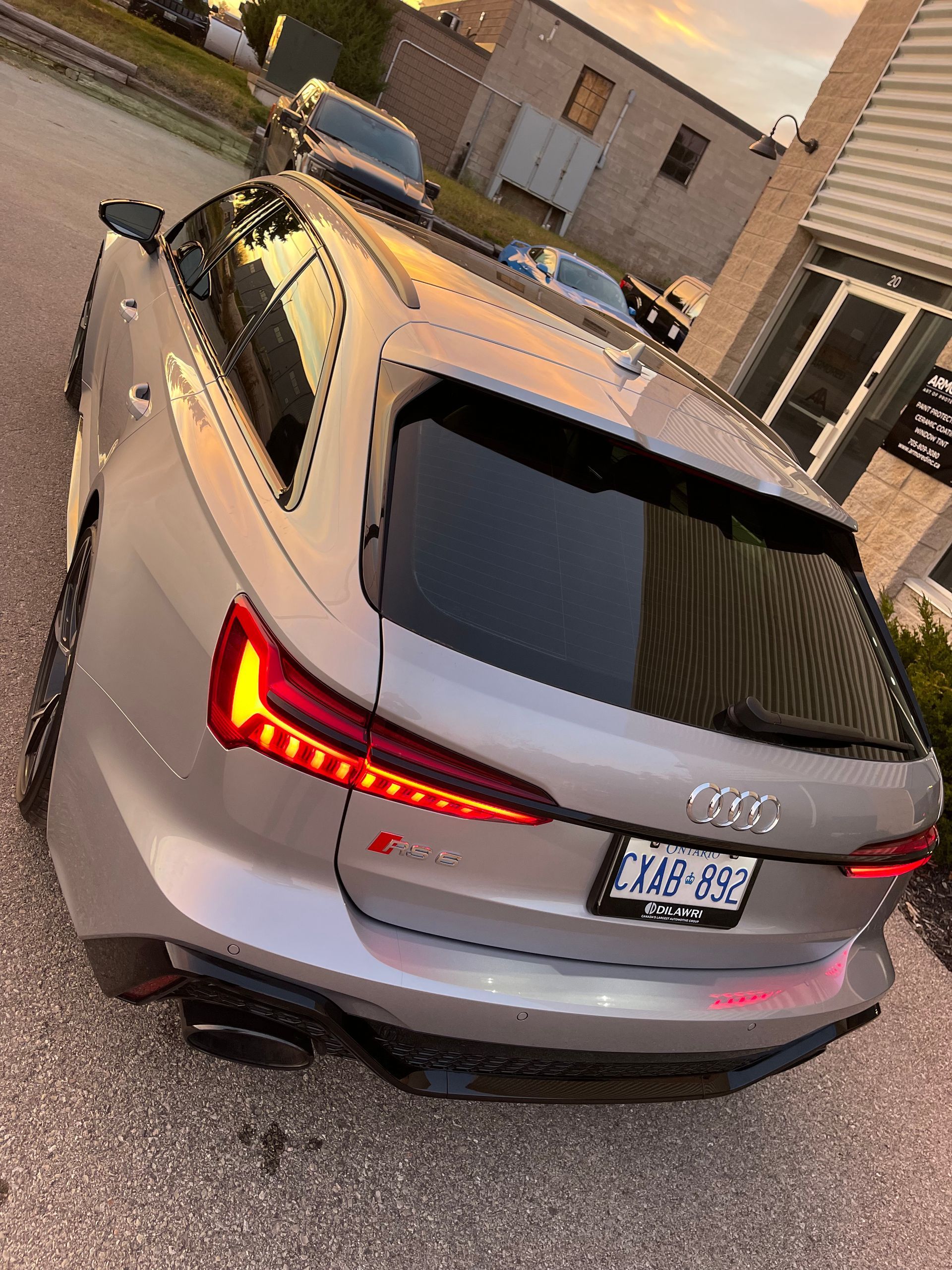 A silver Audi RS6 Avant parked on an asphalt lot at sunset, showcasing its rear lighting and aggressive styling.