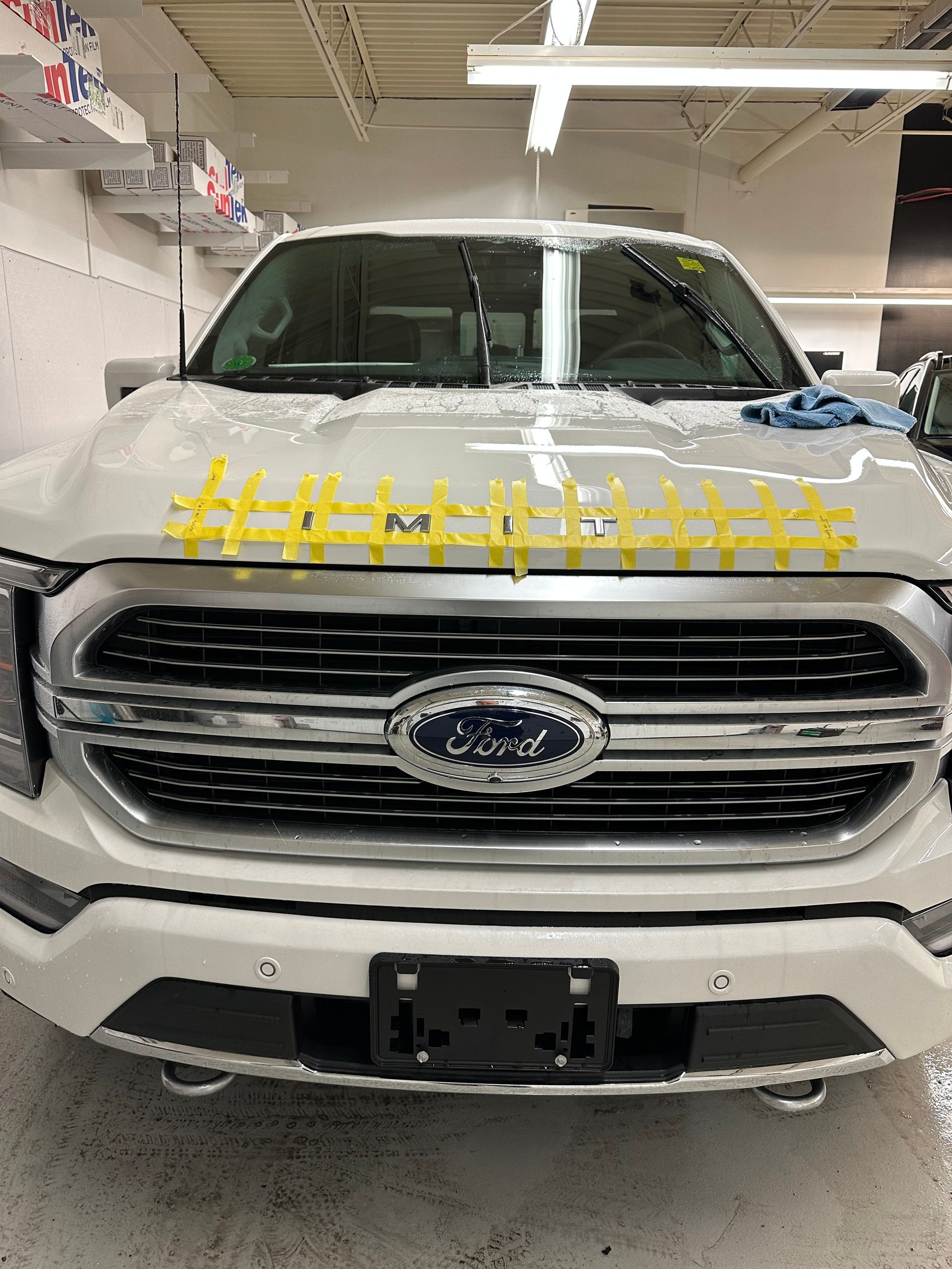 A white Ford pickup truck with yellow tape across the hood, parked inside a garage or shop.