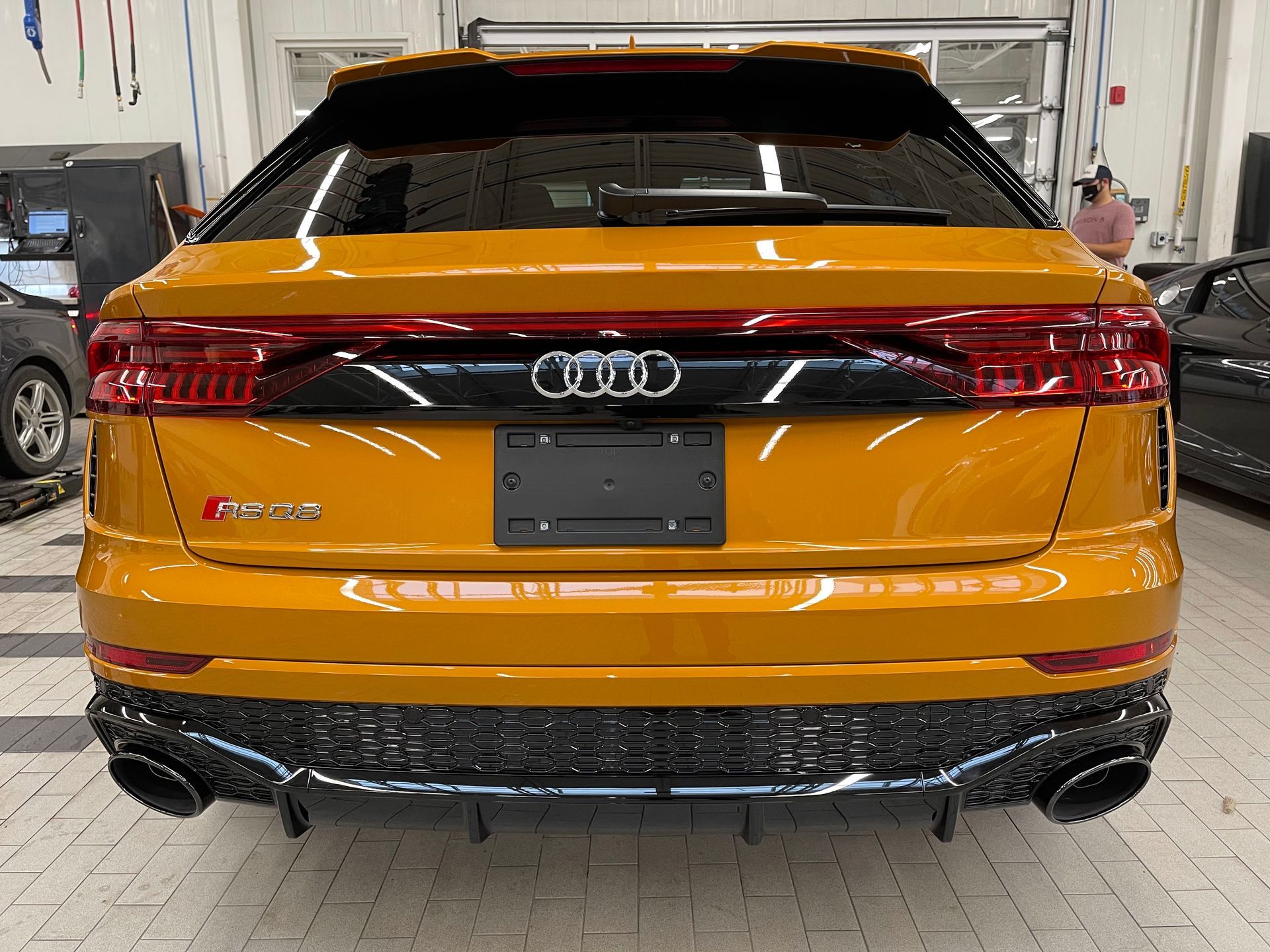 The rear view of a bright yellow Audi RS Q8 with black trim and large exhaust pipes inside a garage.