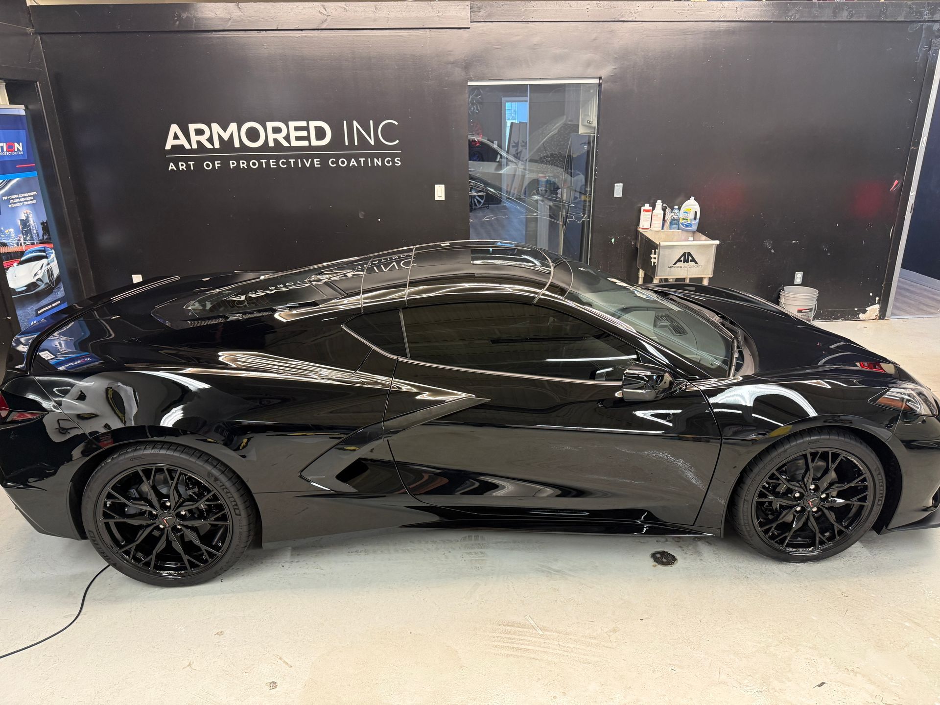 A black Chevrolet Corvette parked inside the Armored Inc. shop, viewed from the side profile.