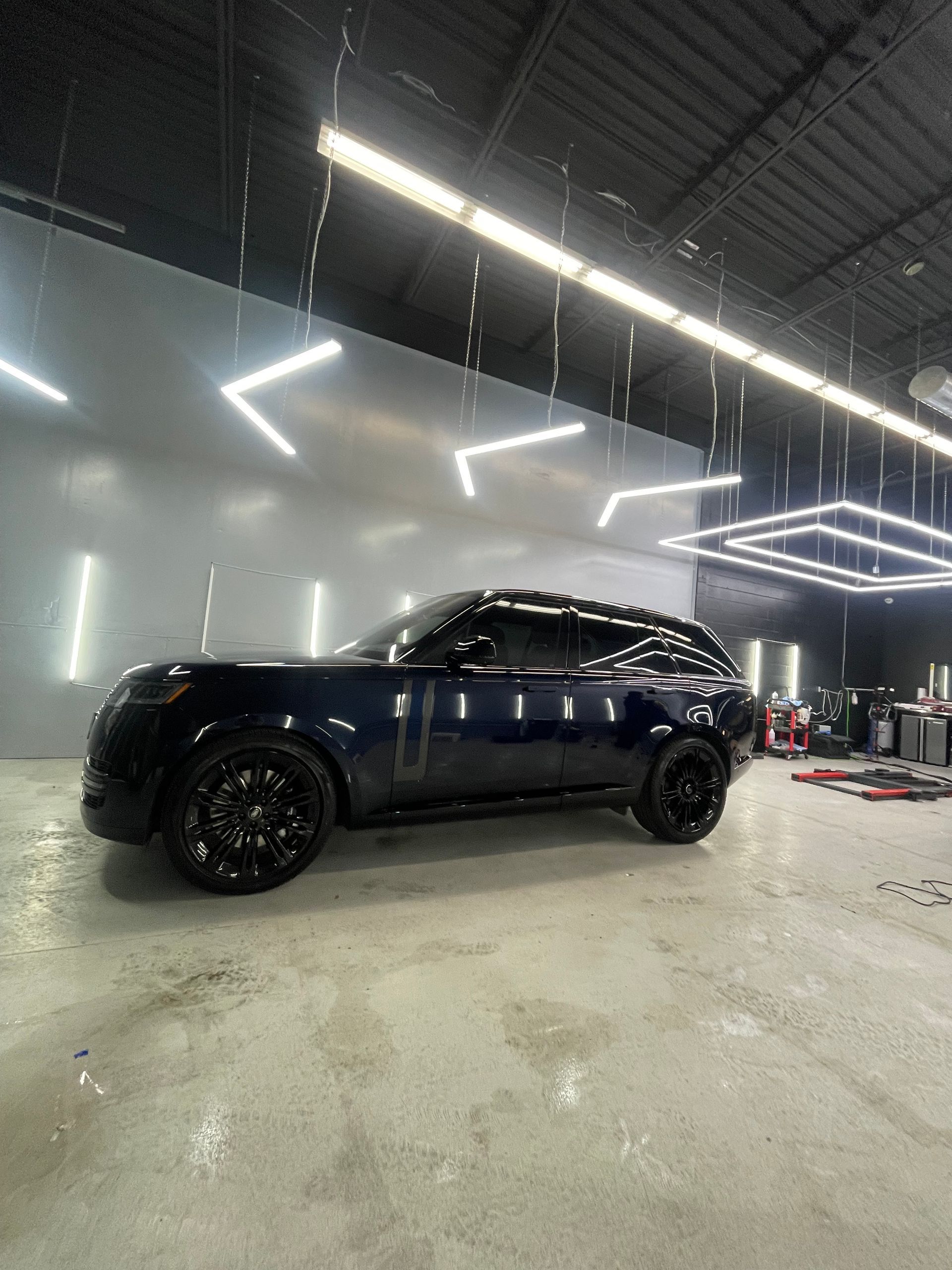 A dark blue SUV with black wheels parked inside a brightly lit professional garage or car detailing shop.