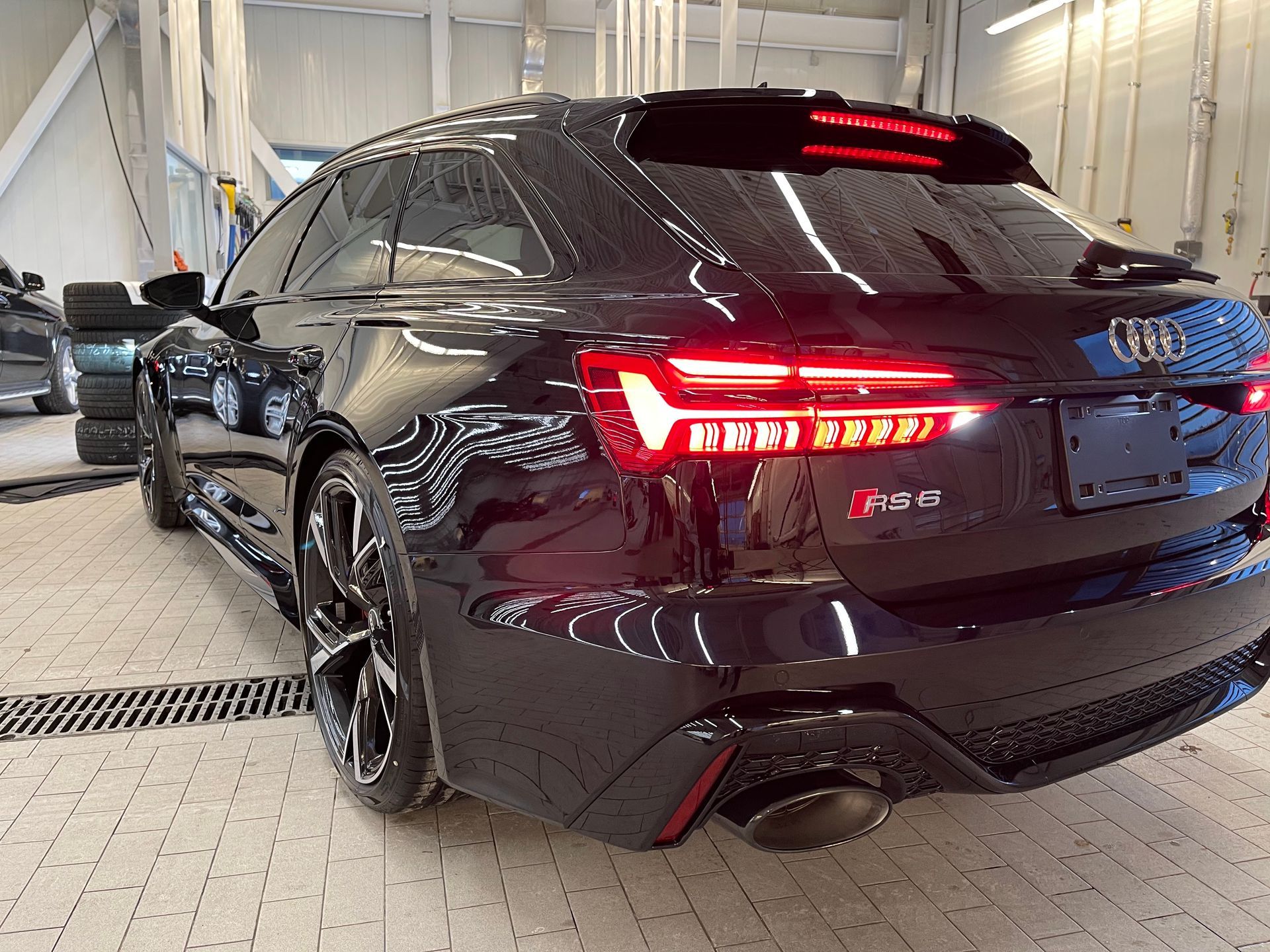 A dark-colored Audi RS 6 Avant parked in a well-lit, industrial garage with tiled flooring.
