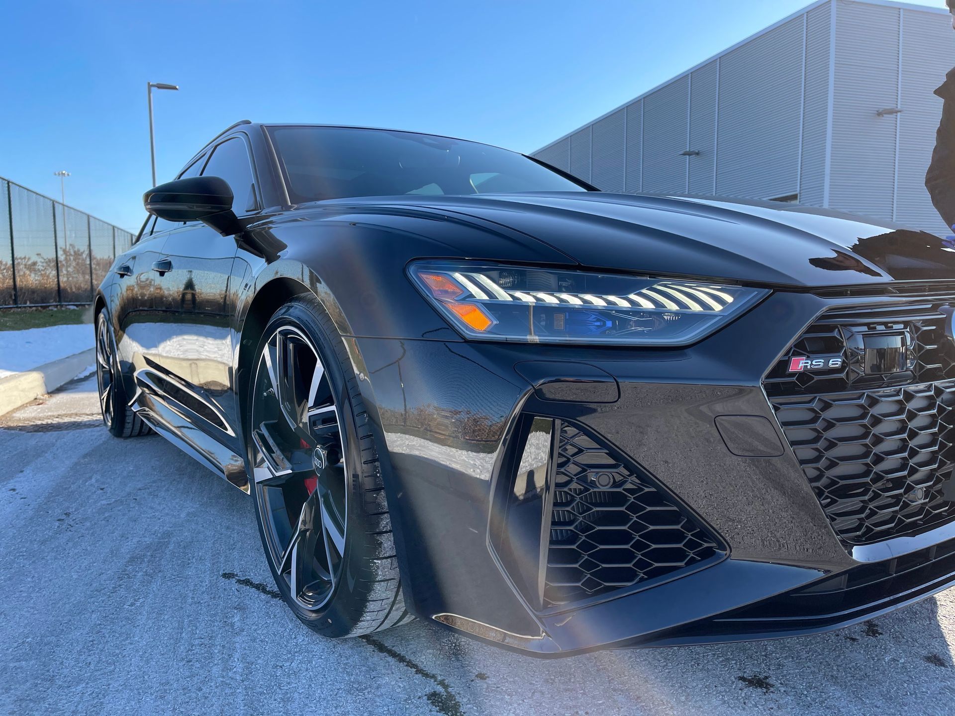 A black Audi RS 6 Avant parked on an asphalt lot under a clear, bright blue sky.