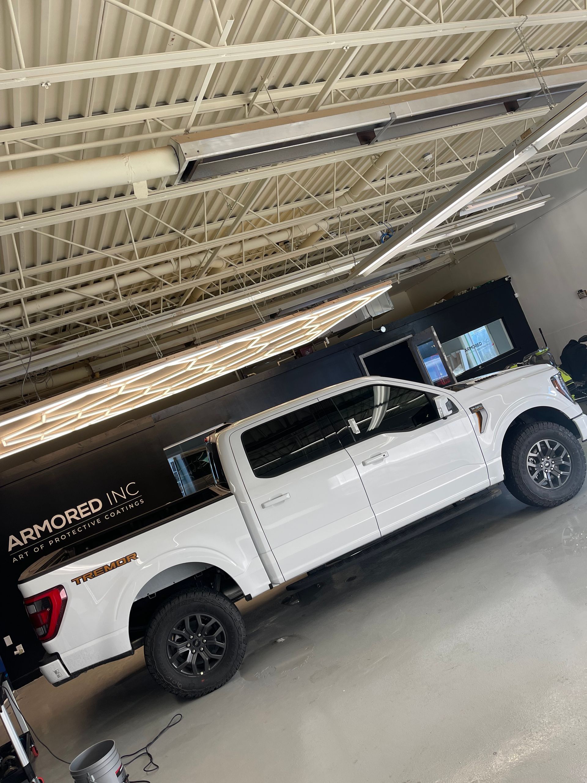 A white Ford F-150 pickup truck parked inside a bright, industrial workshop with a metal corrugated ceiling.