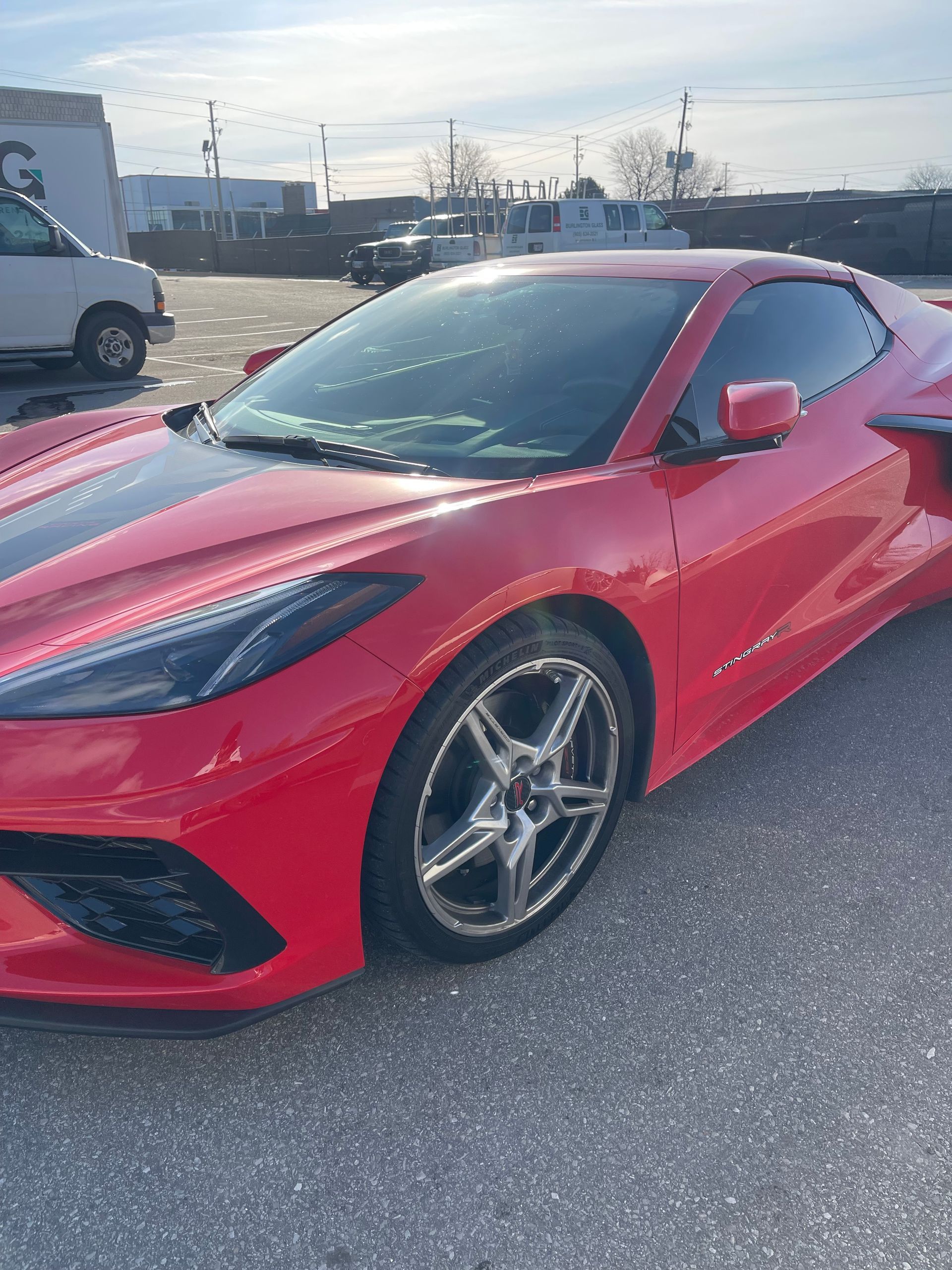 A red Chevrolet Corvette parked on an asphalt lot on a sunny day.
