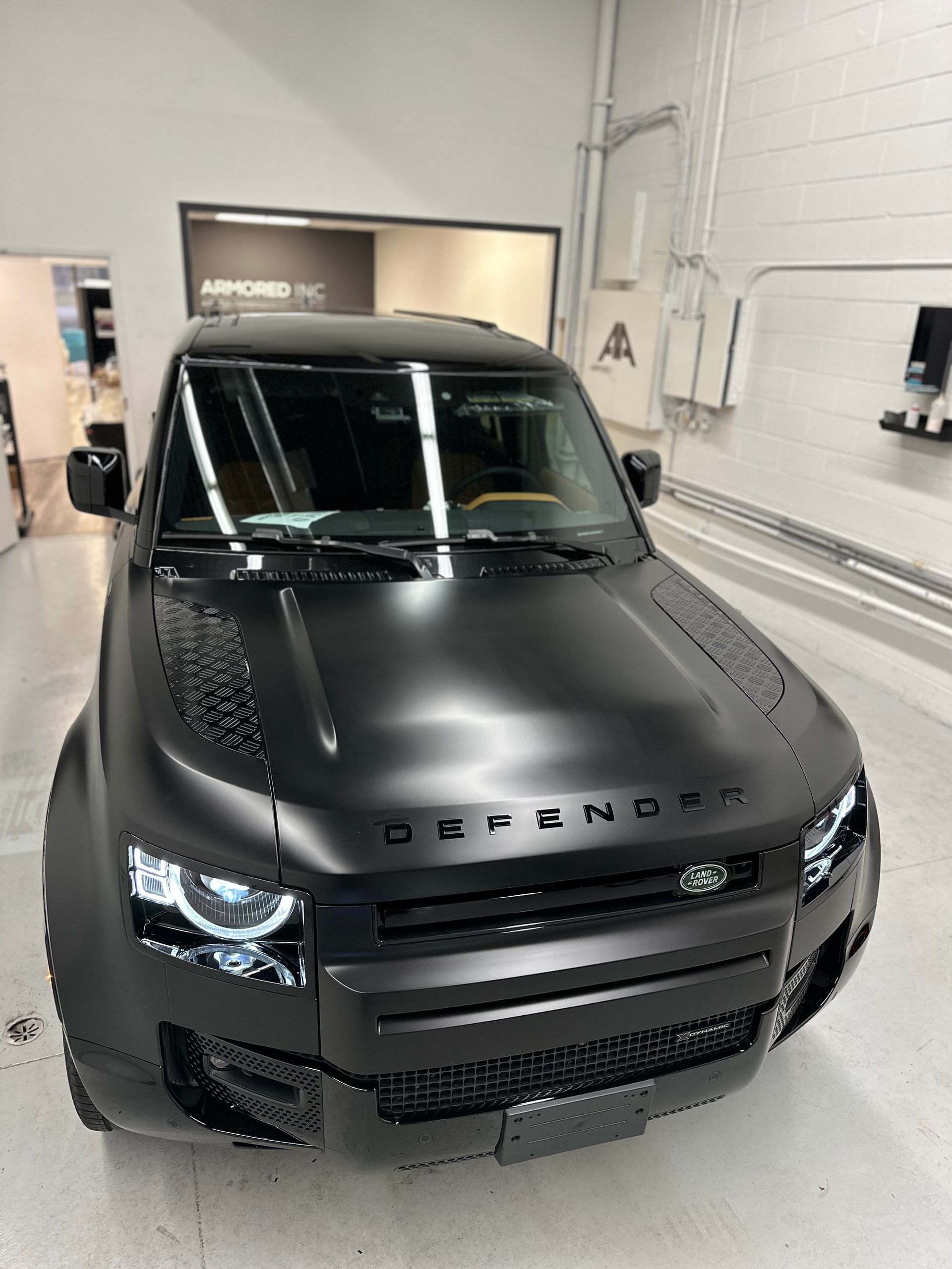 A matte black Land Rover Defender SUV parked inside a garage.