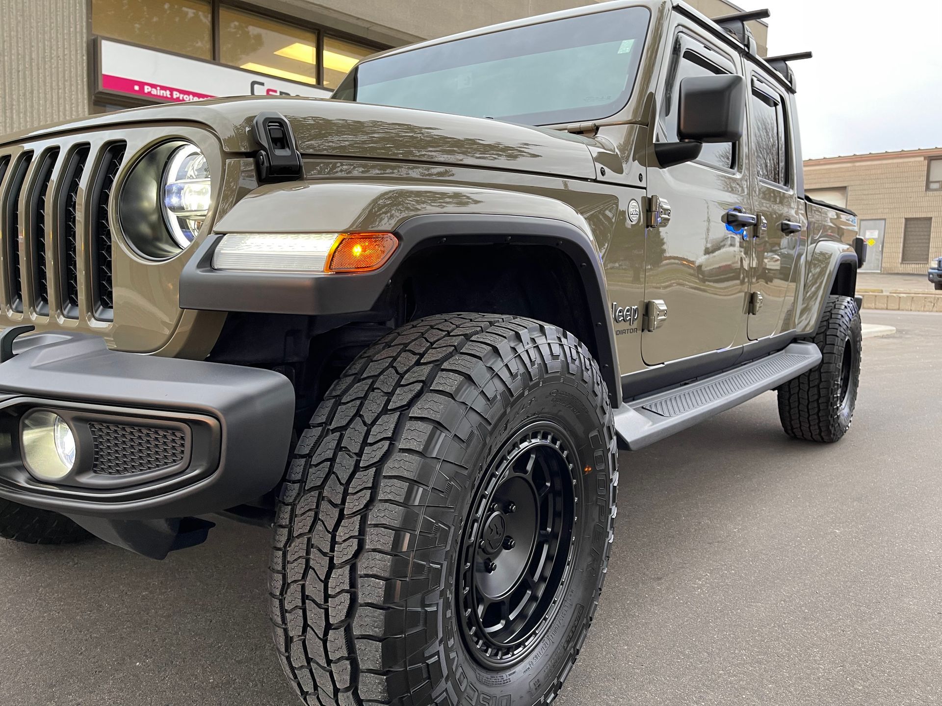 A matte olive green Jeep Gladiator pickup truck parked on an asphalt lot.
