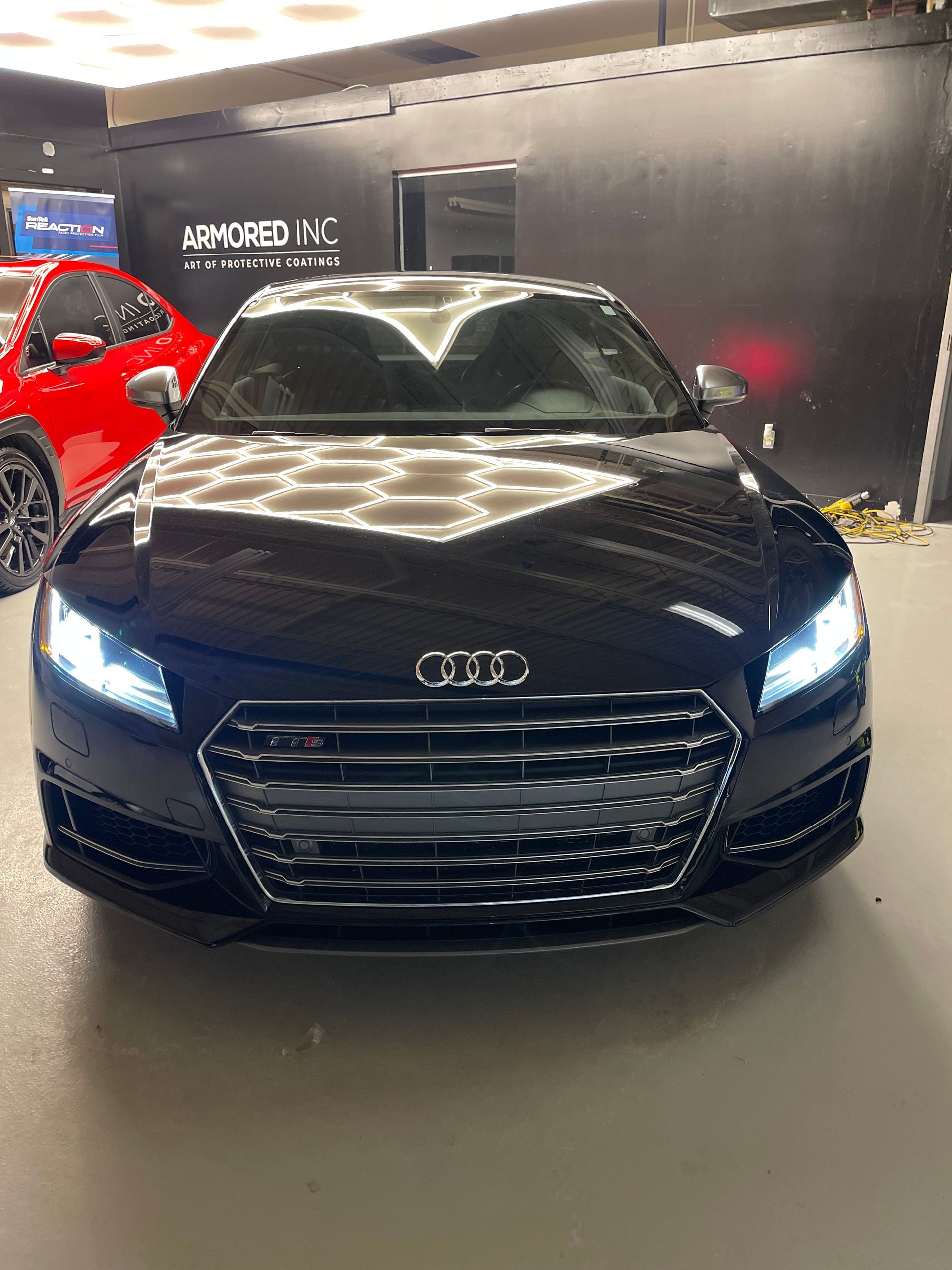 A front-facing black Audi sports car parked inside a garage with bright overhead lighting.