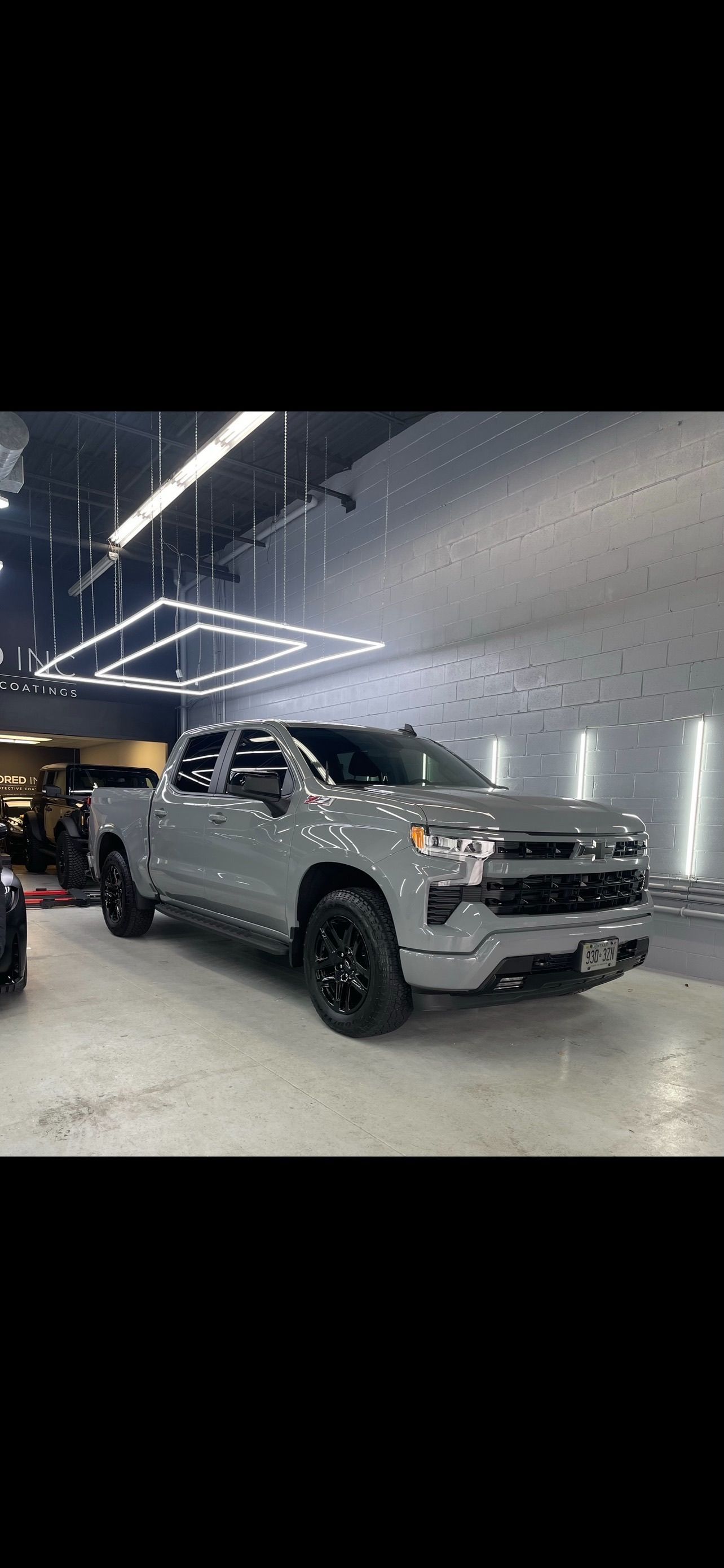 A grey crew-cab pickup truck with black wheels parked inside a brightly lit professional automotive shop.