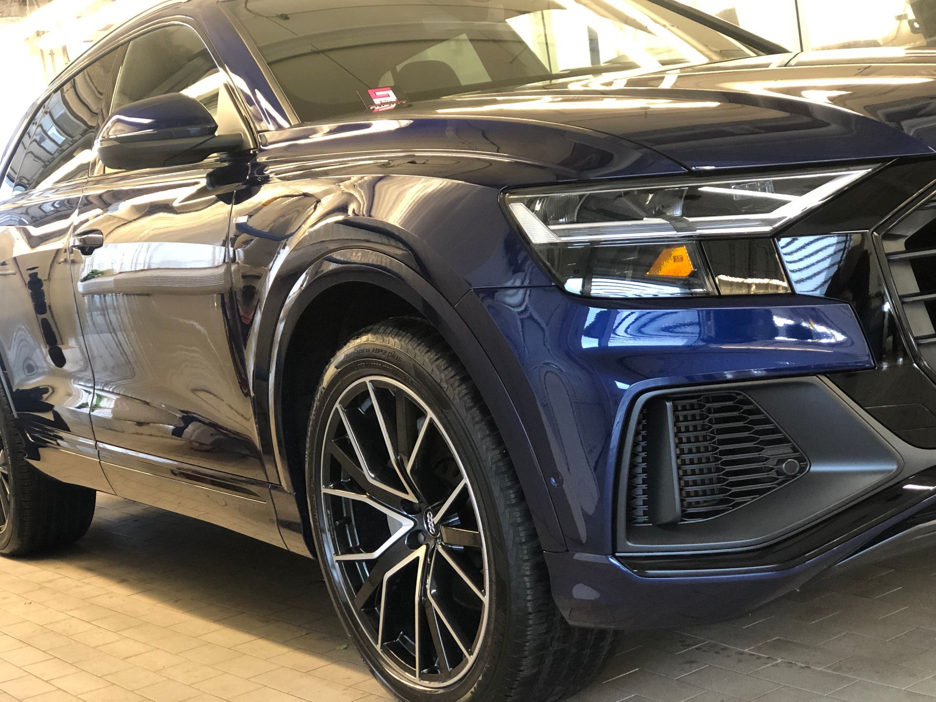 A dark blue Audi Q8 SUV parked indoors, featuring distinctive multi-spoke alloy wheels and sharp LED headlights.