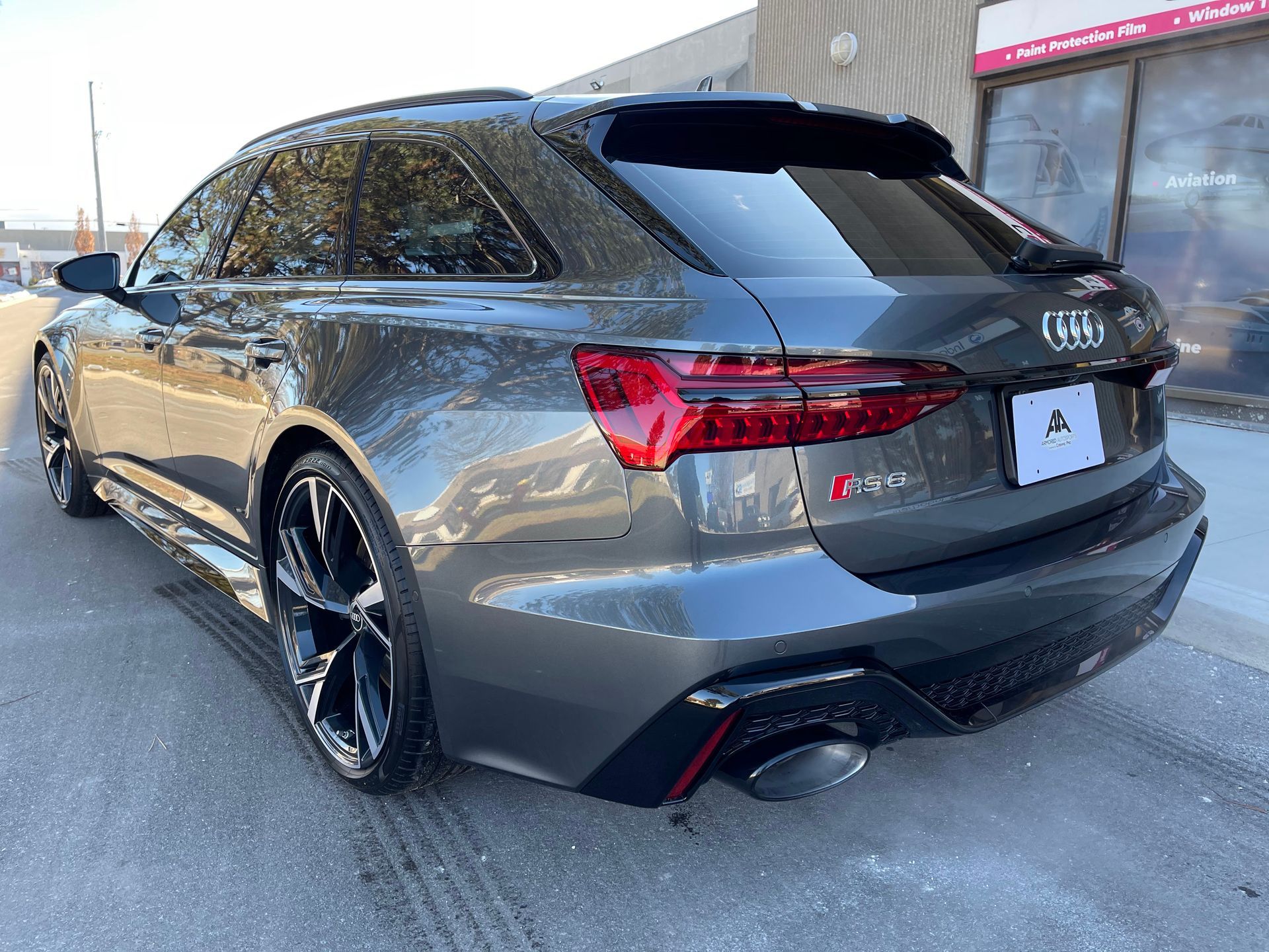 A grey Audi RS6 Avant station wagon parked on a paved lot, angled from the rear driver's side to show the taillights.