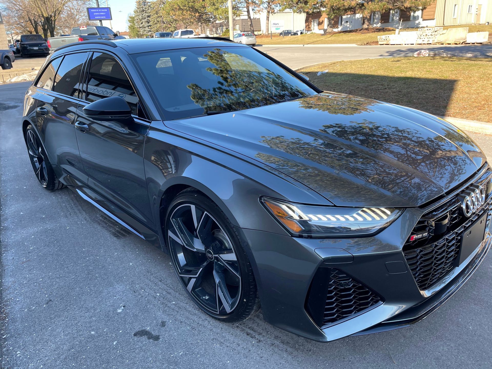 A dark gray Audi RS6 Avant wagon parked on a sunny paved surface.