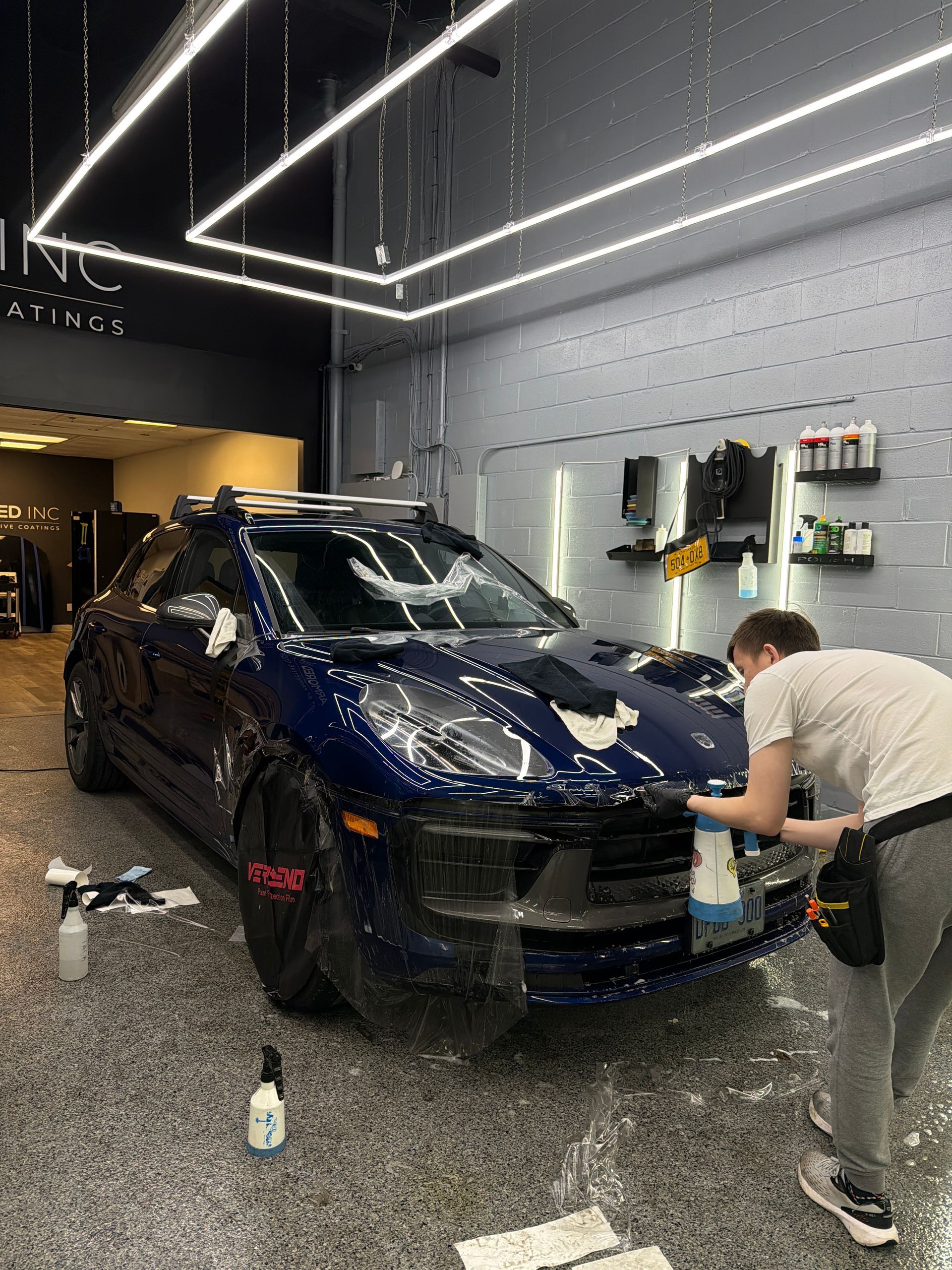 A person detailing a dark blue SUV inside a well-lit, professional automotive workshop.