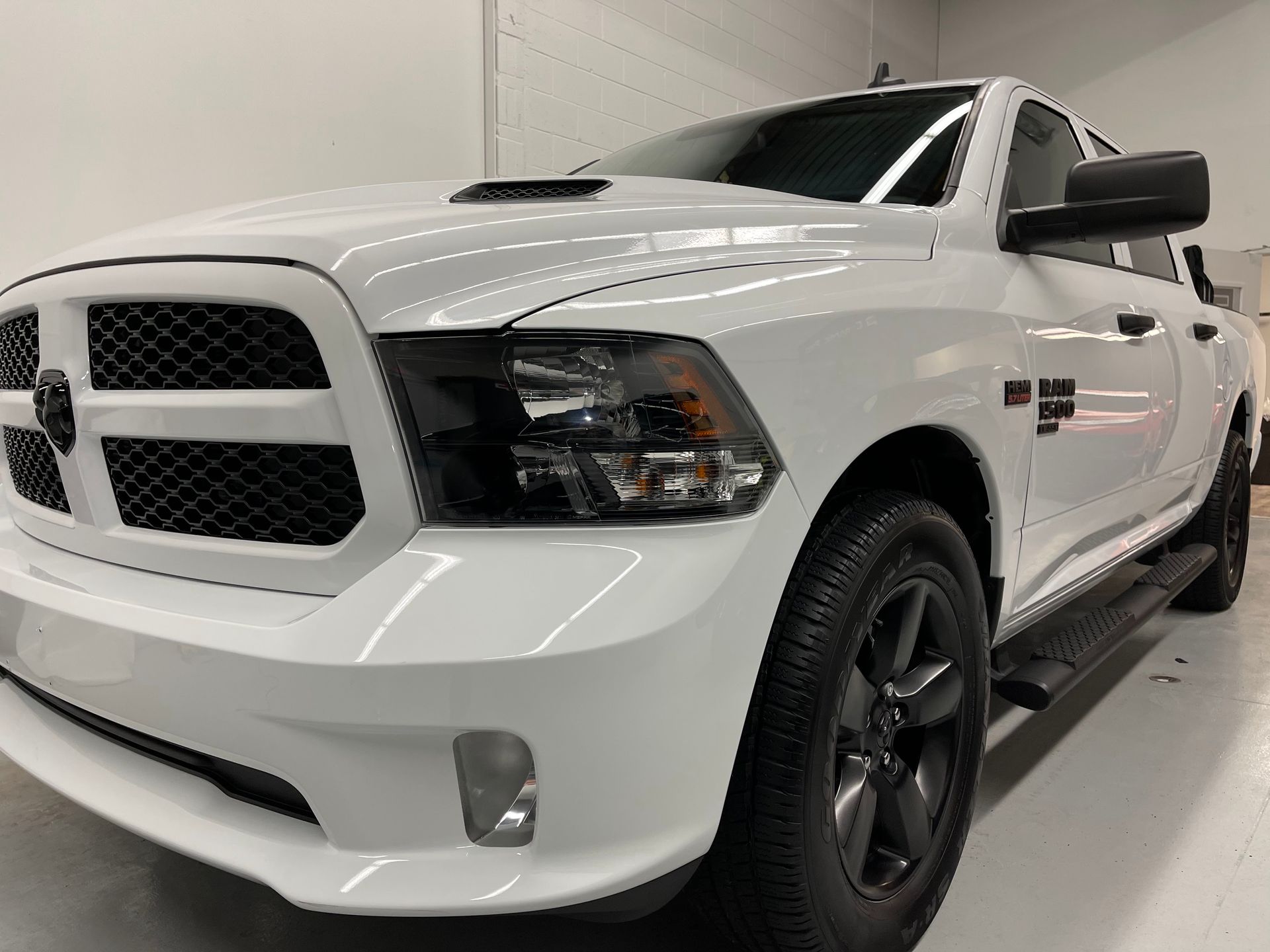 A white Ram 1500 pickup truck with black trim and wheels parked in a bright, indoor garage.