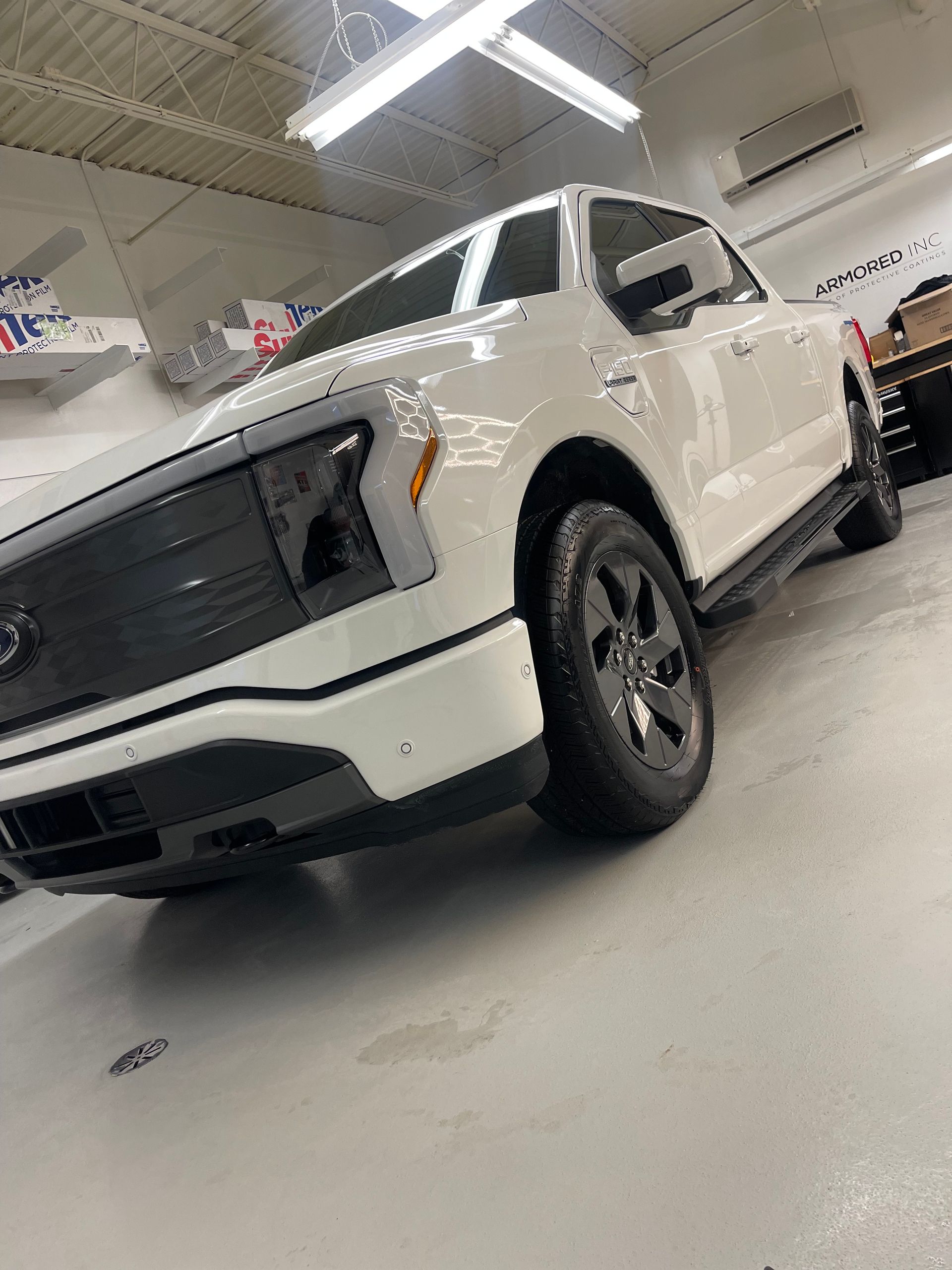A white Ford F-150 Lightning pickup truck parked on a light-colored floor inside a garage.
