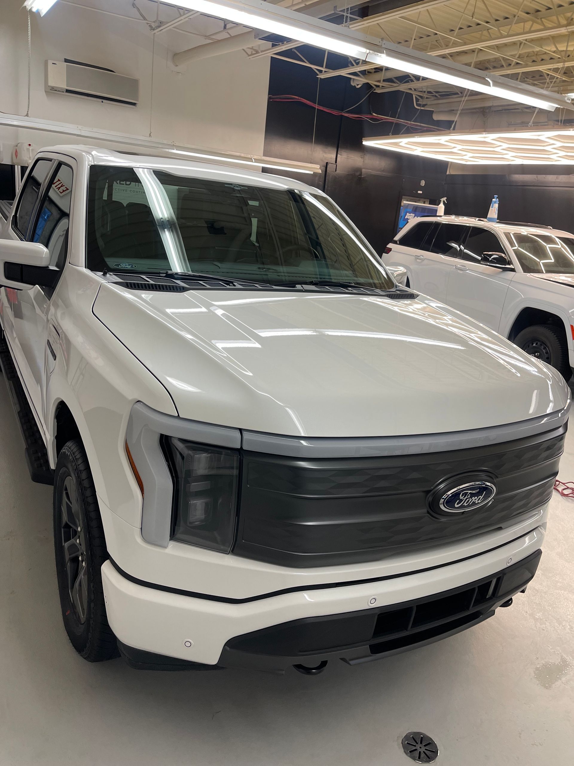 A white Ford F-150 Lightning pickup truck parked inside a brightly lit automotive shop or garage.