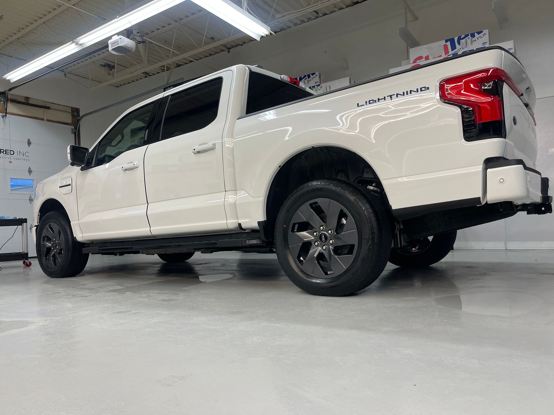 A white Ford F-150 Lightning pickup truck parked in a bright, clean garage with dark rims.