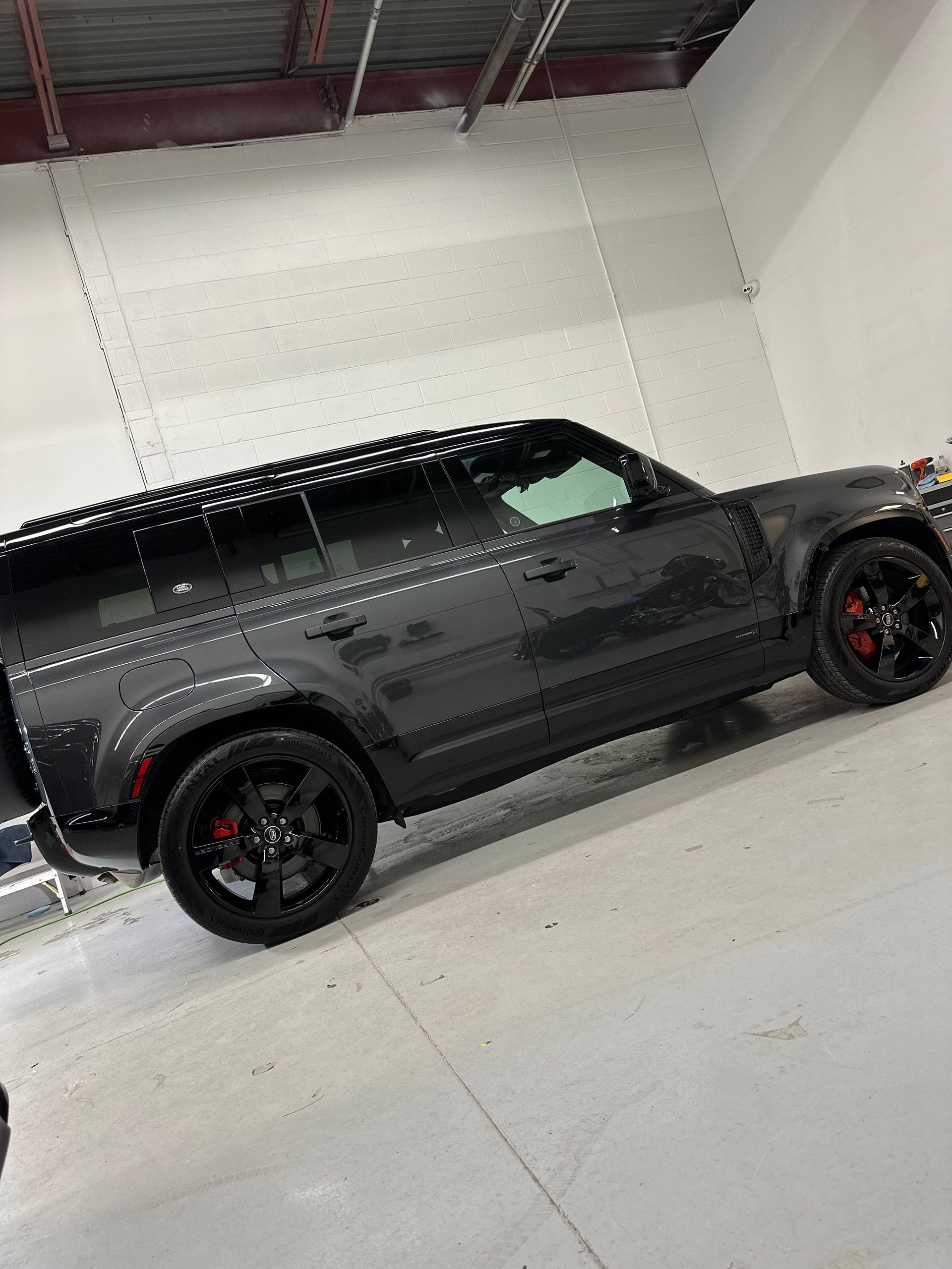 A dark gray Land Rover Defender SUV parked inside a garage, featuring black wheels with red brake calipers.