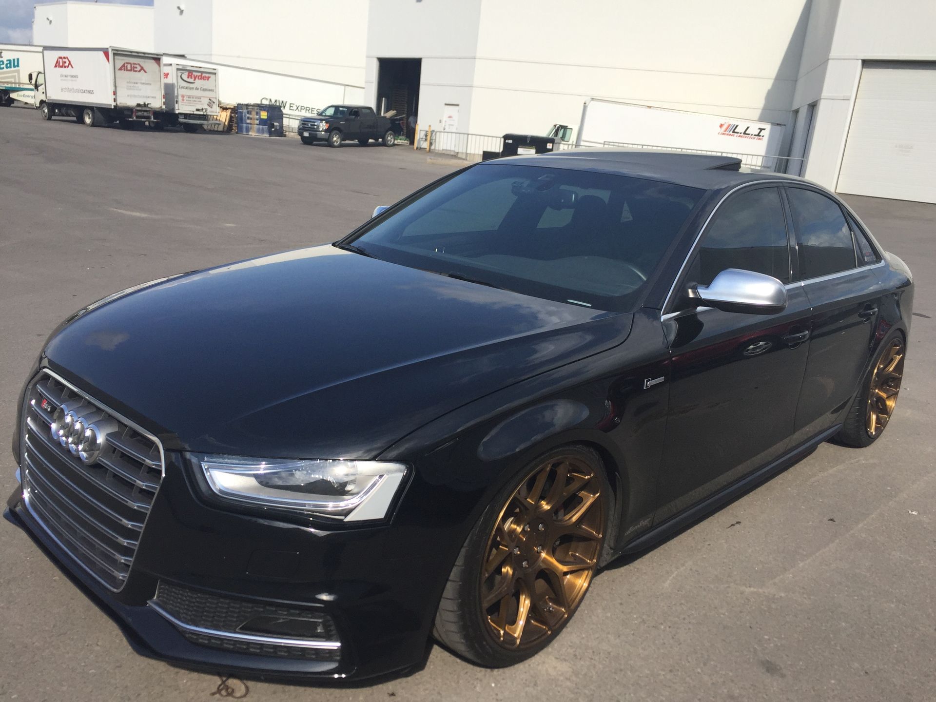 A black Audi sedan with metallic bronze wheels, parked in an asphalt lot.