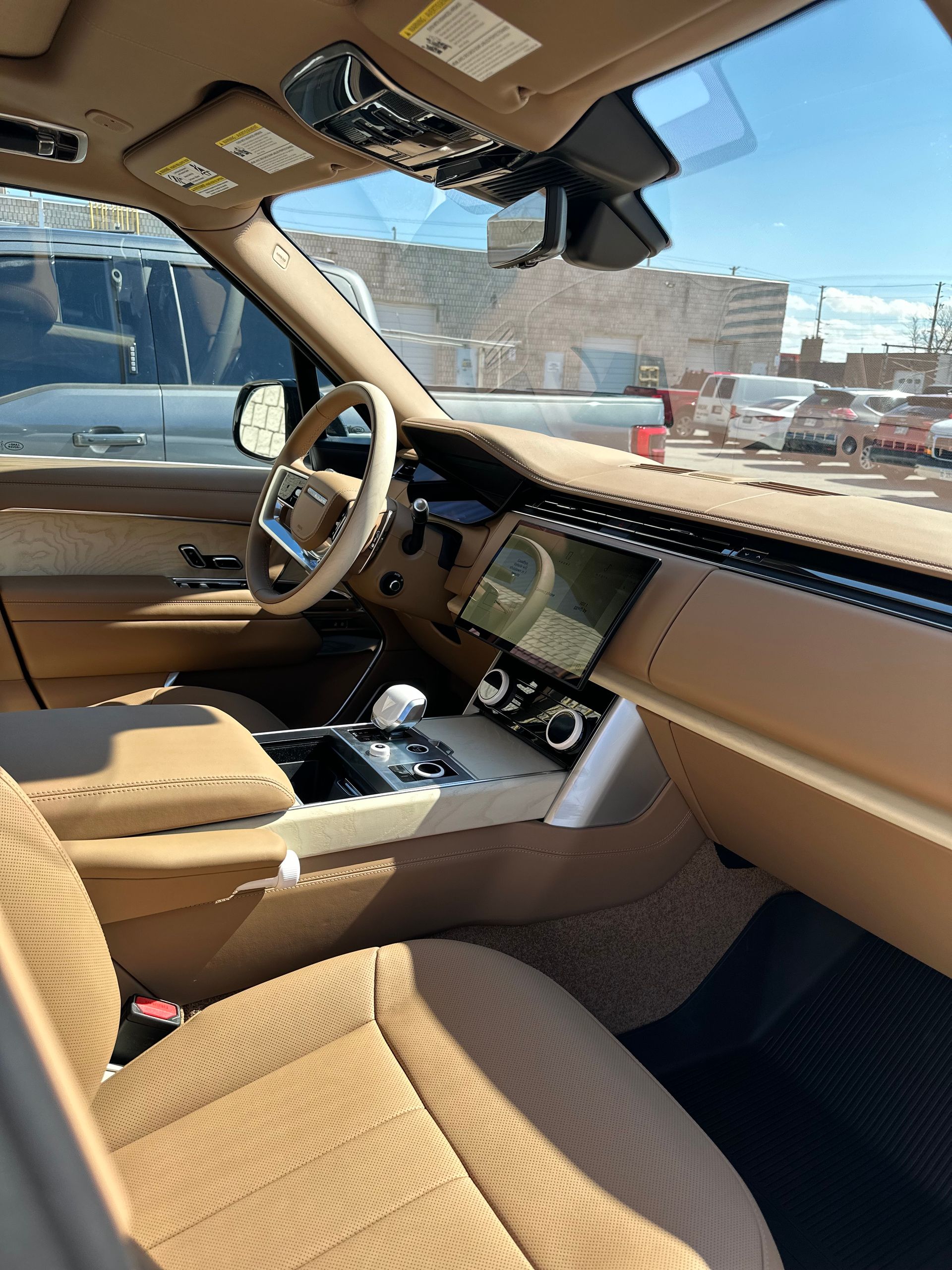 The interior of a vehicle featuring tan leather upholstery, a digital dashboard, and a view through the windshield.