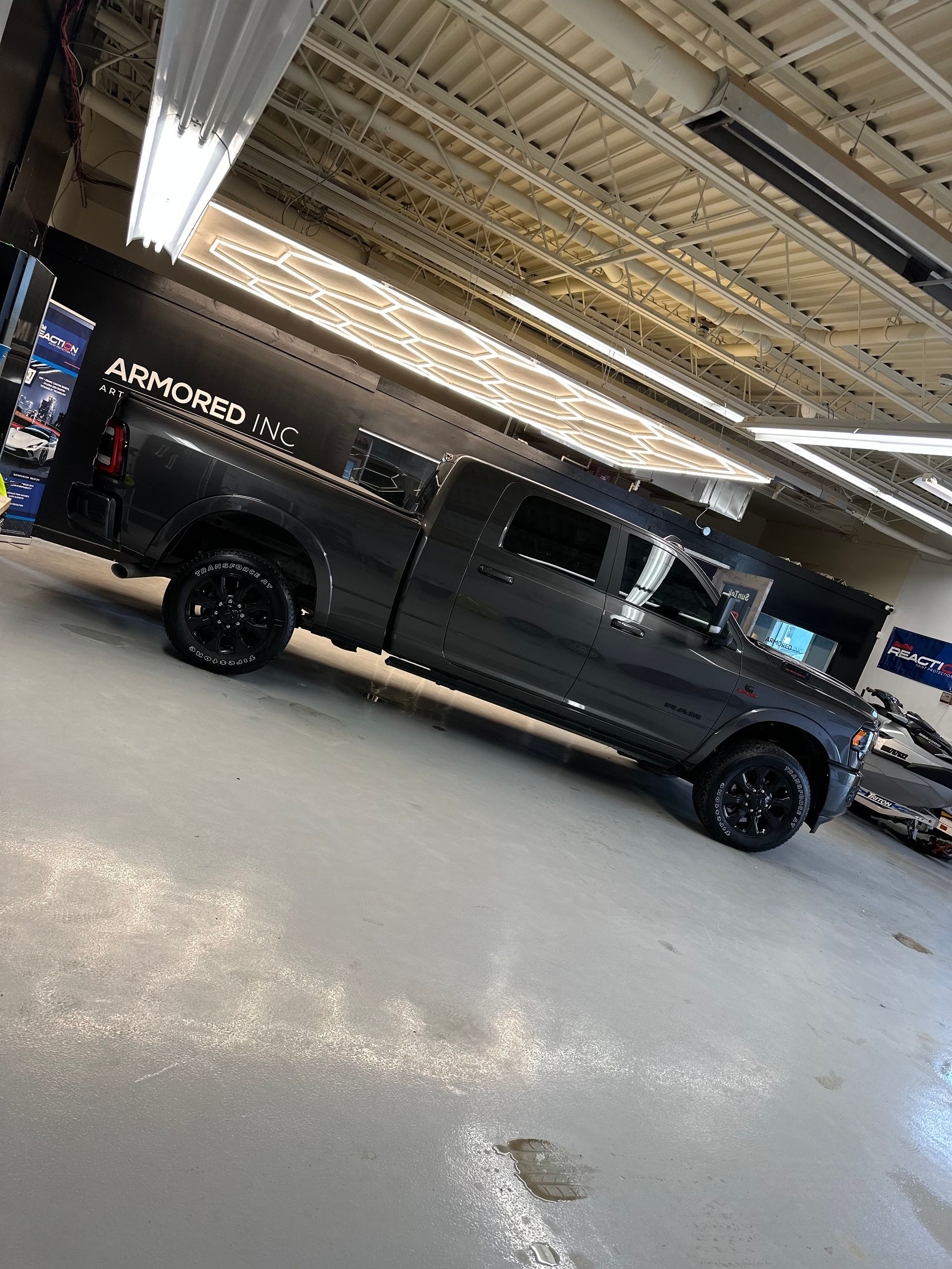 A dark-colored, four-door pickup truck parked inside a bright, industrial garage with overhead lights.