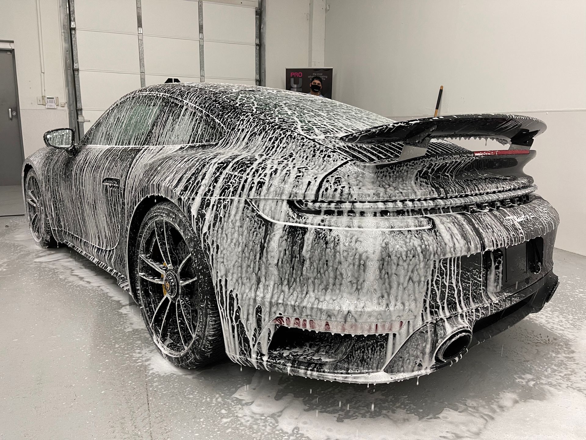 A dark sports car covered in thick white cleaning foam, parked inside a garage.